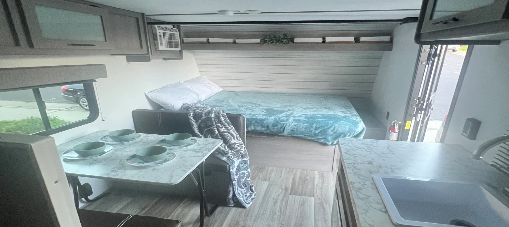 Experience comfort in this RV rental, featuring a cozy bed, dinette with dishes, kitchen sink, and overhead storage.. Dutchmen Coleman Lantern LT 2024