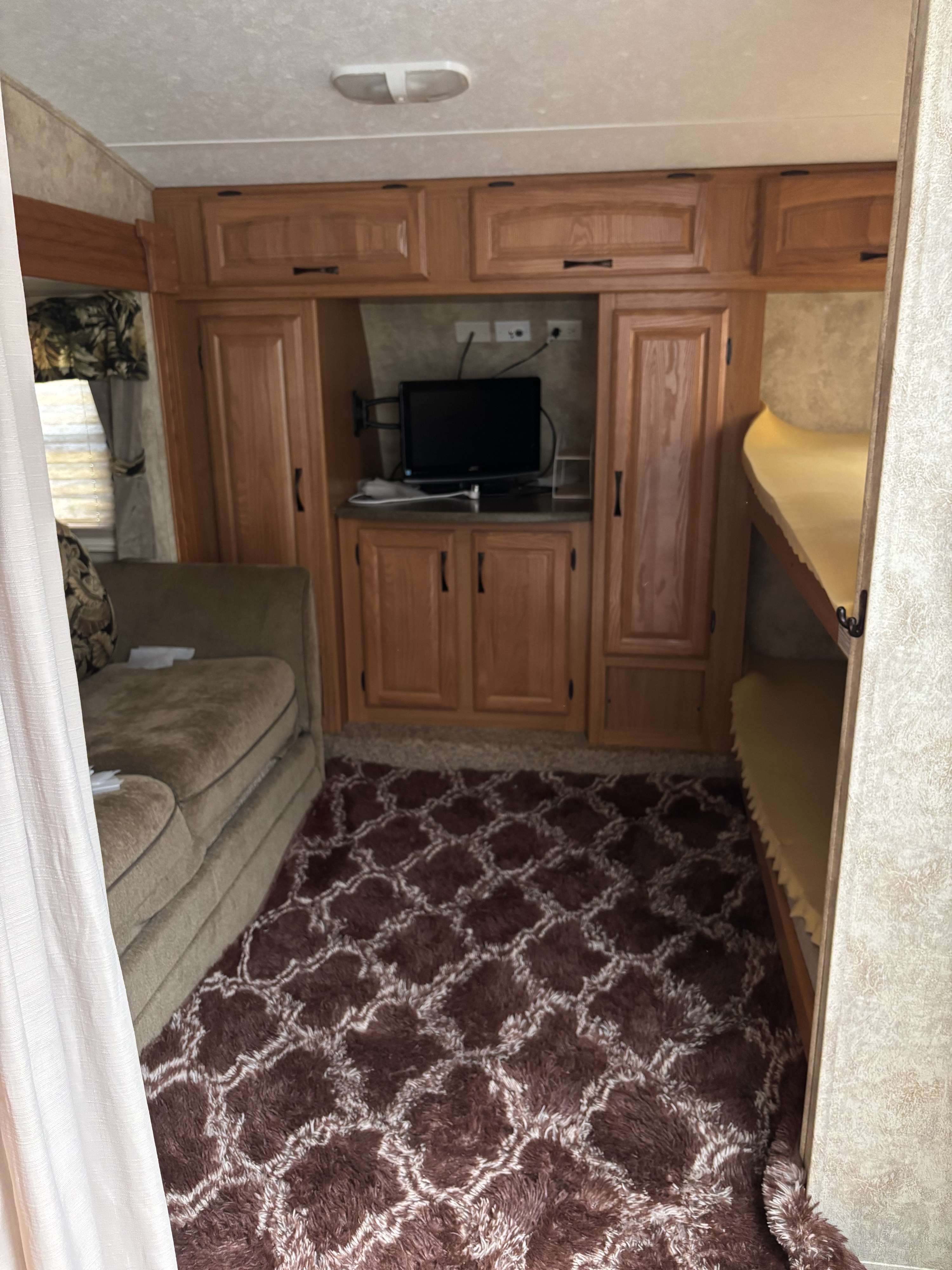 Step inside this RV rental featuring a comfortable couch, wooden entertainment center with TV, and convenient bunk beds, all on a patterned rug.. Keystone RV Laredo 2007