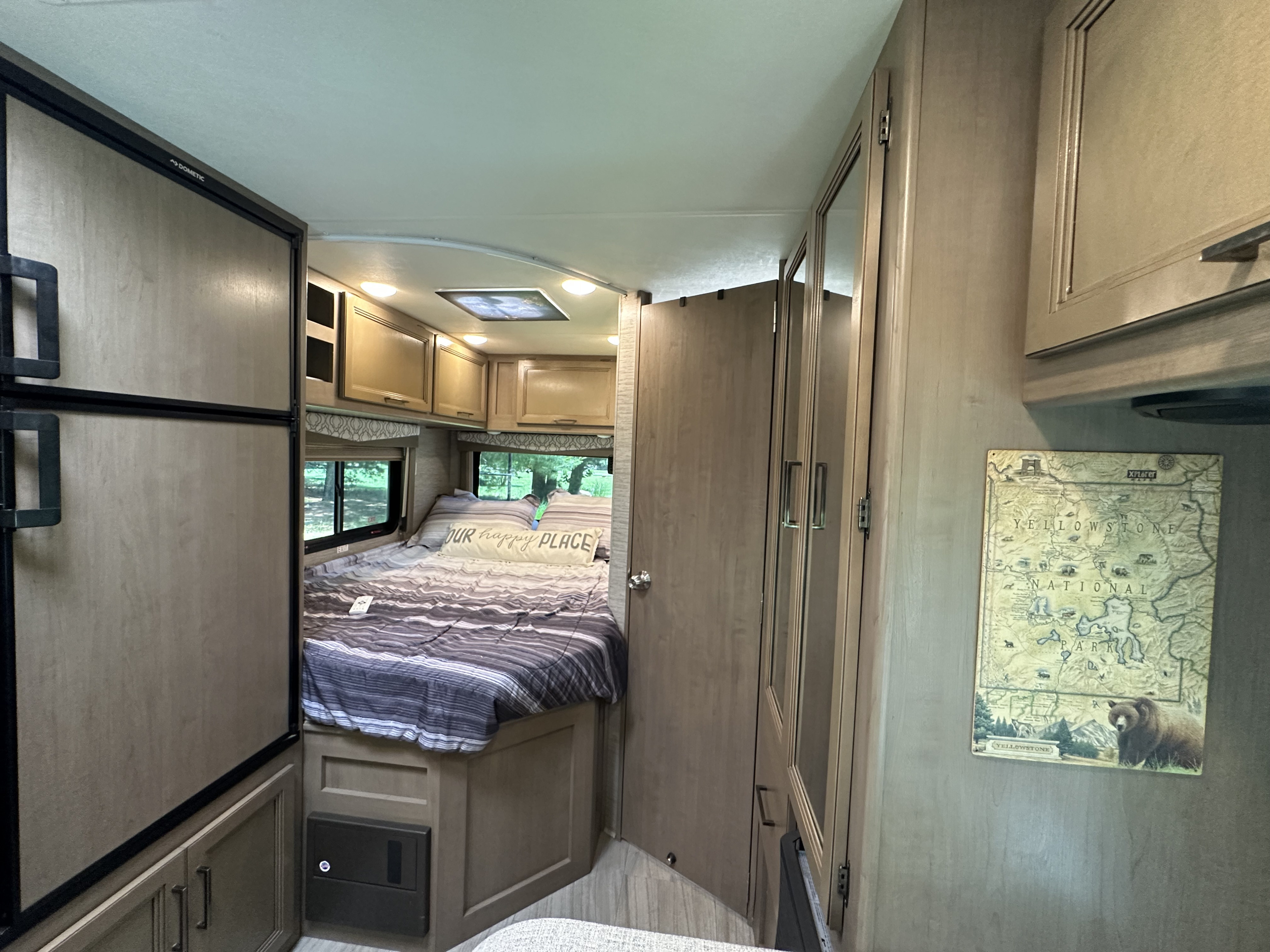Experience RV rental comfort: a bedroom with a striped bed, windows, fridge, and storage. Ready for adventure!. Thor Quantum SE 2021