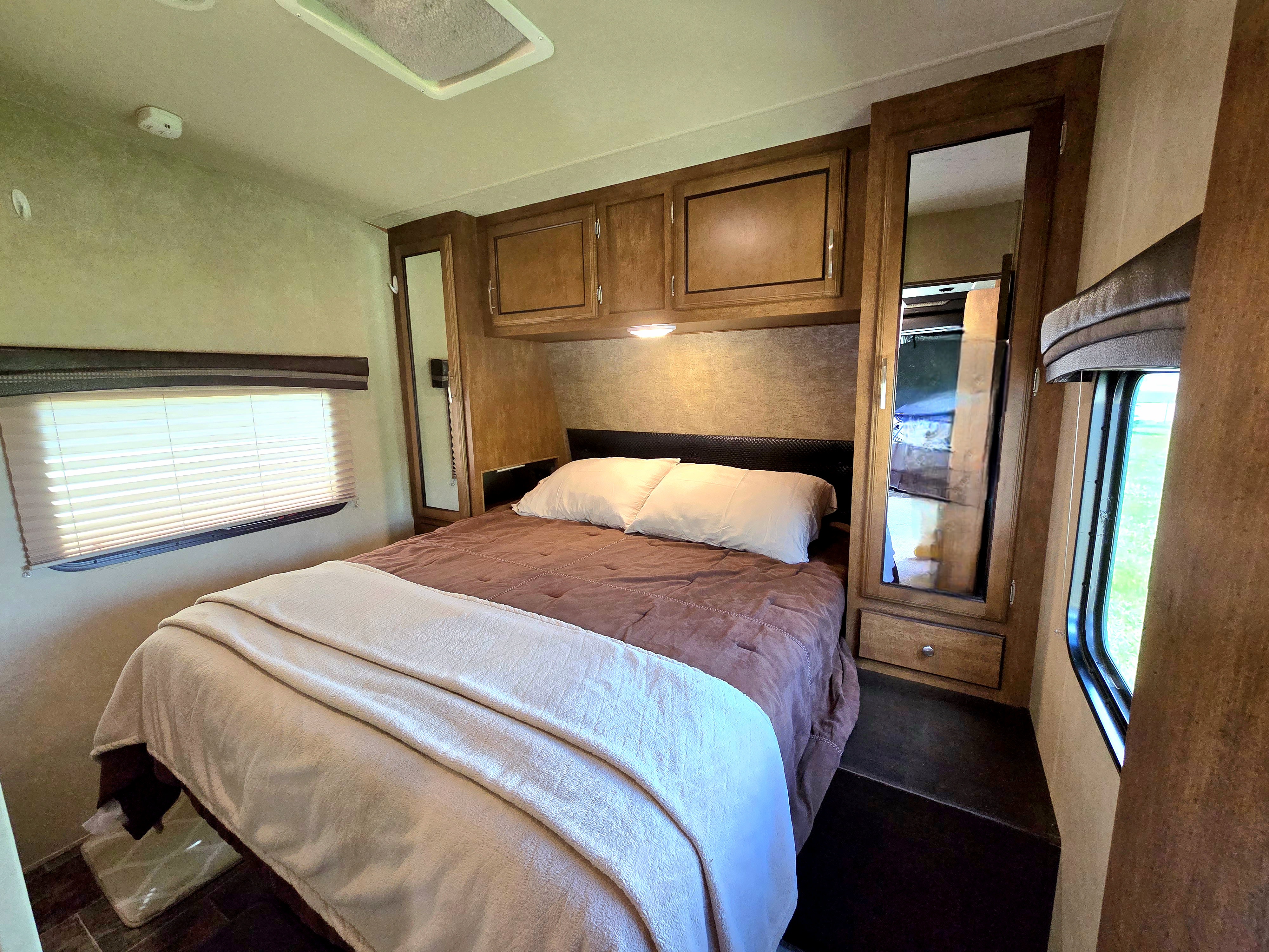 Comfortable RV rental bedroom featuring a bed, storage cabinets, and mirrored closets for a cozy travel stay.. Forest River Shockwave 2017