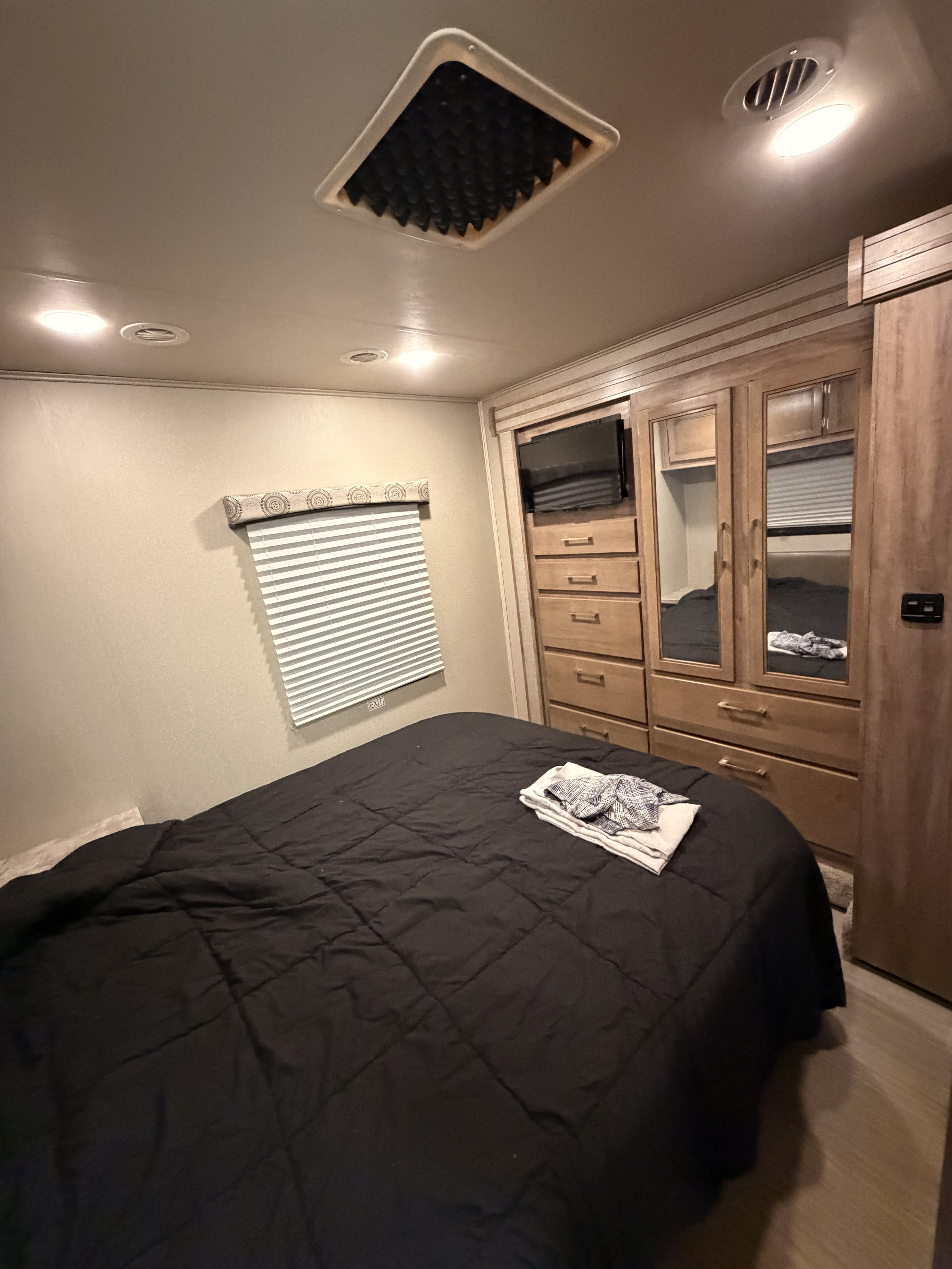 Inside an RV rental bedroom: a black-comforter bed, blinds, TV, and mirrored wardrobe offer compact comfort.. Entegra Coach Odyssey 2020