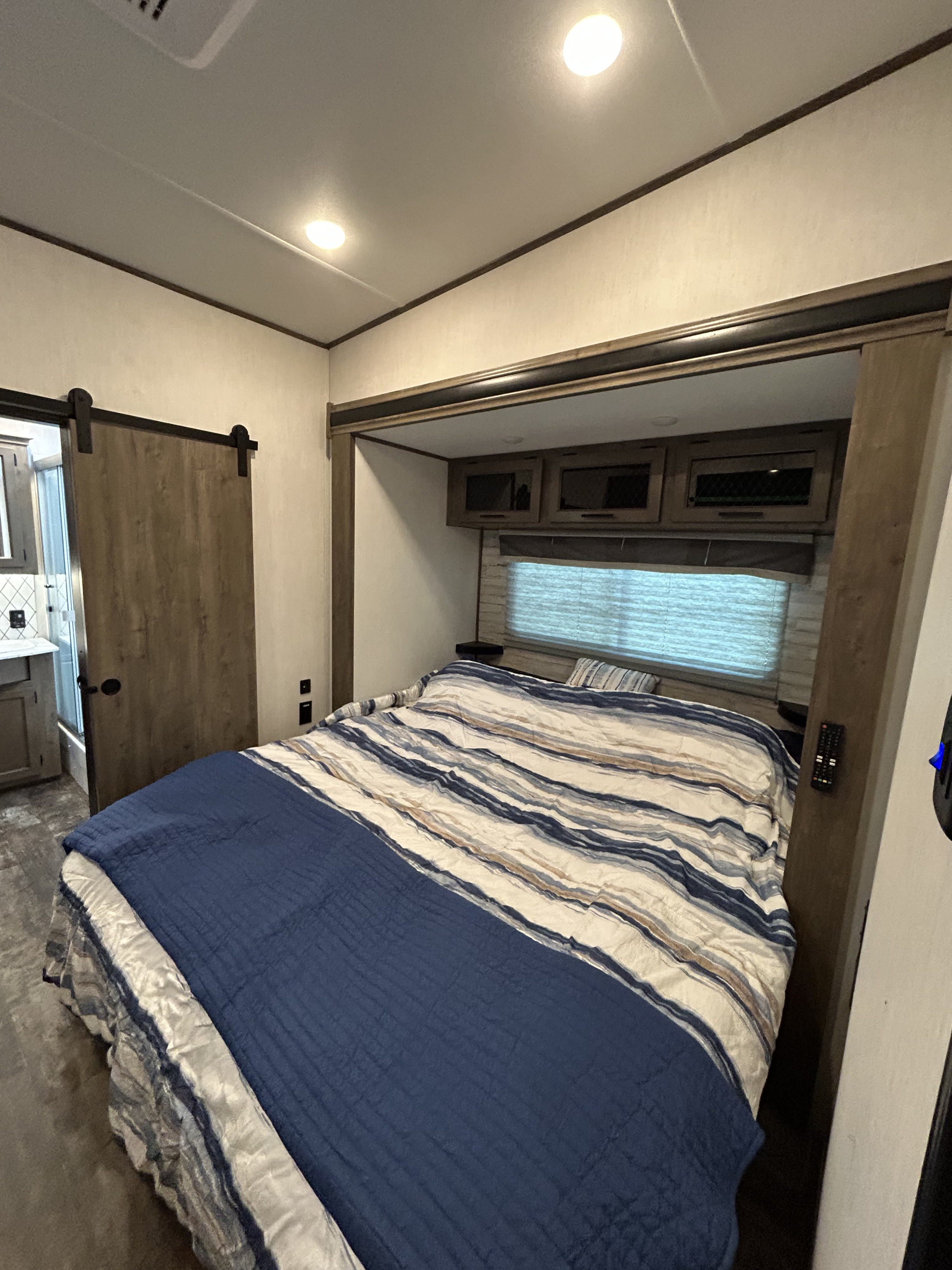 Cozy RV rental bedroom features a comfy bed with blue & striped bedding, overhead storage, and a barn door to the bathroom.. Forest River Sabre 2022