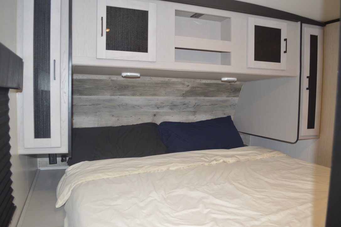 RV rental bedroom interior with cozy bed, wooden headboard, and overhead storage cabinets. Ideal for travel and adventure.. Heartland RVs Mallard 2023