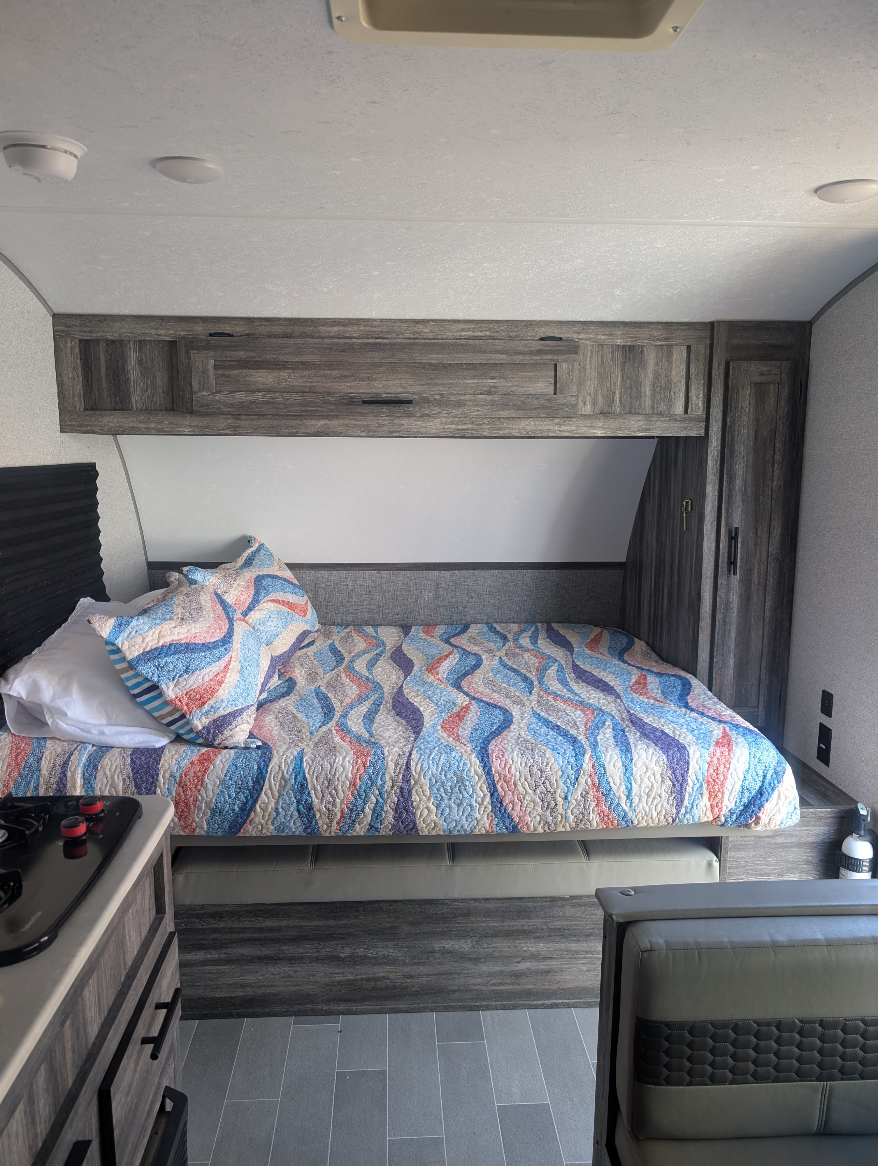 Relax in this cozy RV rental's bedroom, featuring a vibrant patterned quilt, practical overhead cabinets, and a nearby kitchen view.. Forest River Wildwood FSX Plantium 2022
