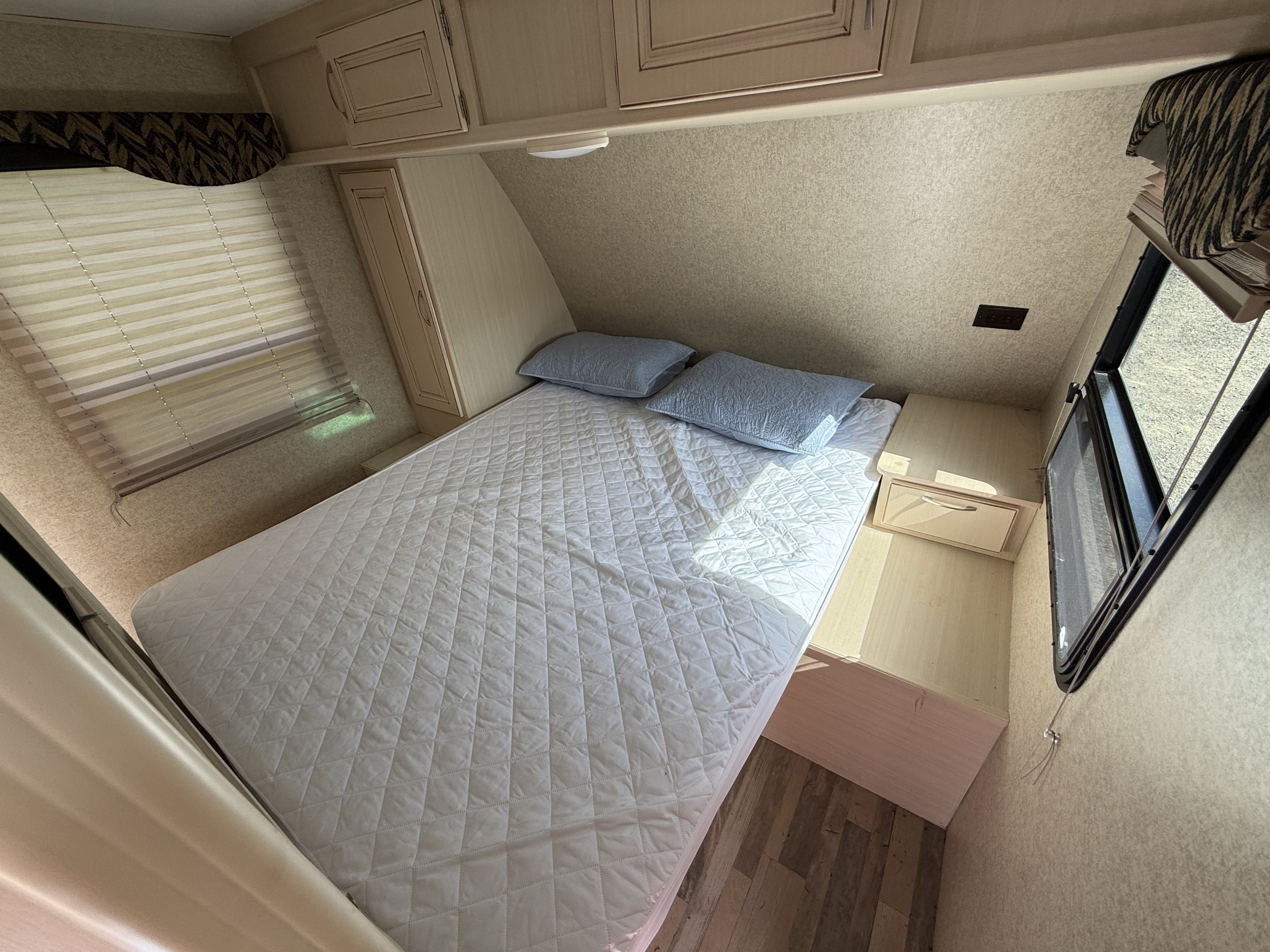 Cozy RV rental bedroom with a quilted bed, light blue pillows, overhead cabinets, and windows for natural light.. Winnebago Minnie 2455BHS 2017