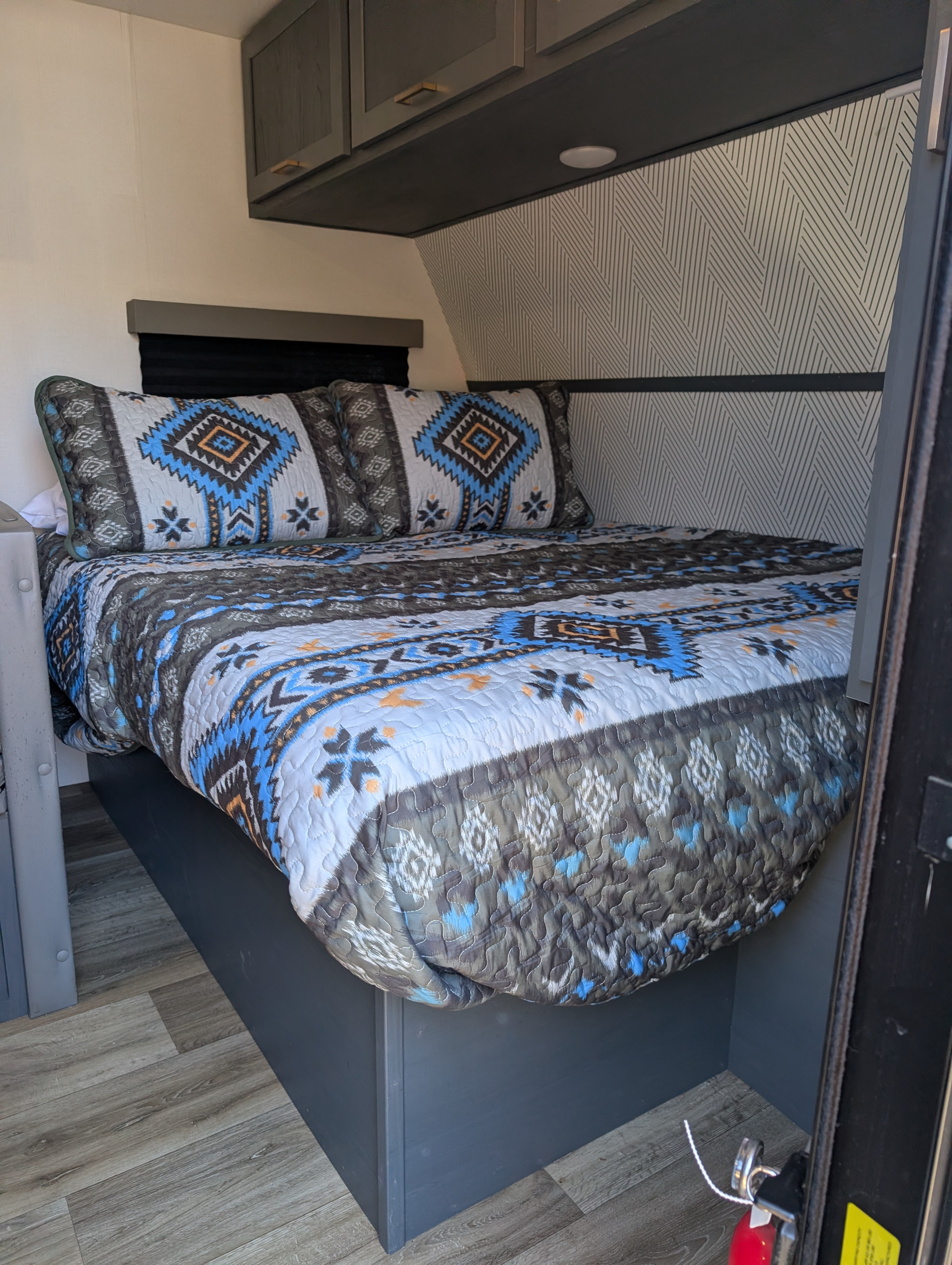 RV rental bedroom: A cozy bed with a geometric patterned quilt, gray cabinets, and a modern accent wall.. Keystone RV Bullet Crossfire 2021