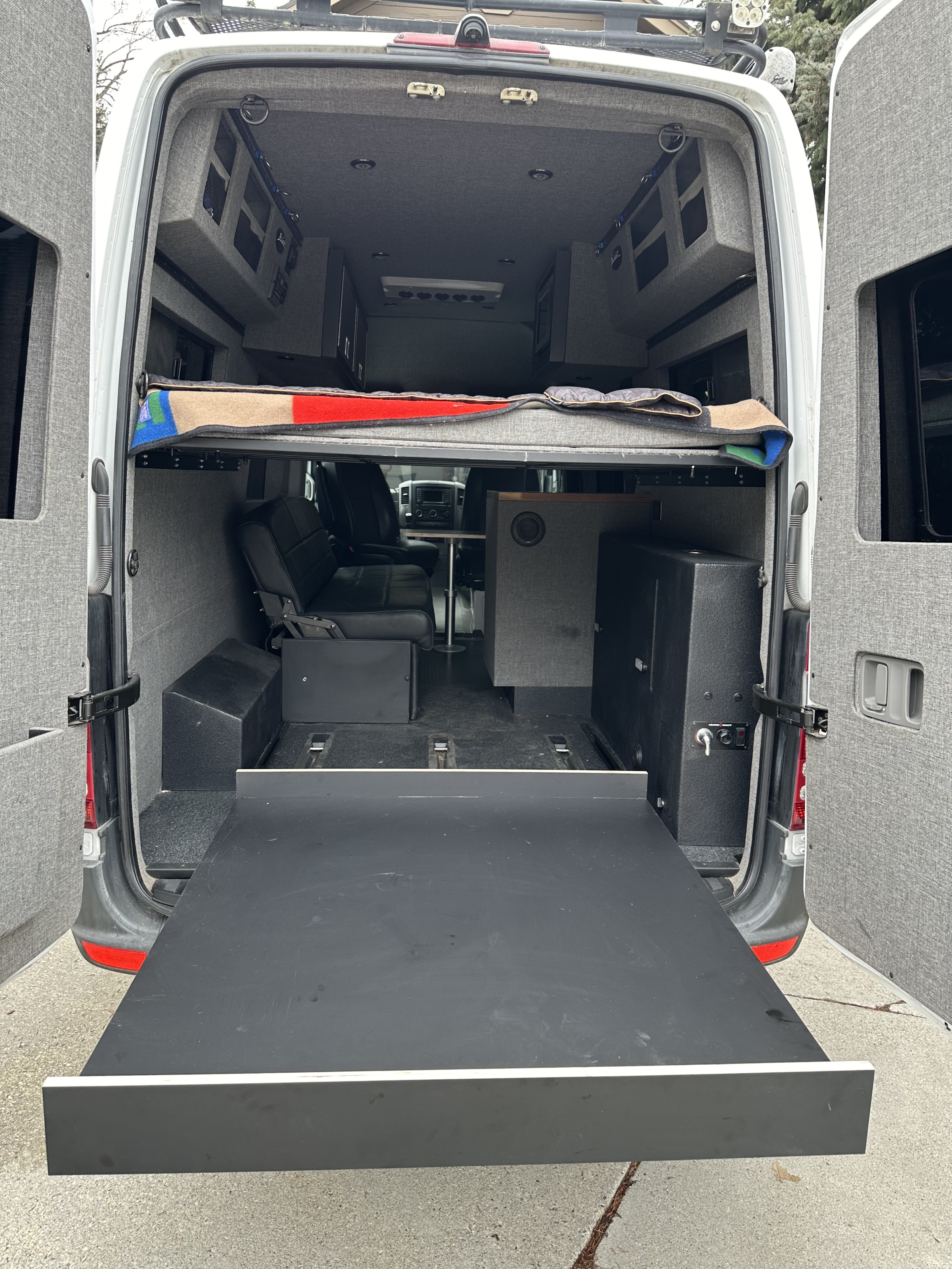 Rear view of an rv rental camper van conversion: elevated bed, seating, storage, and a large pull-out tray.. El Kapitan Sprinter 2500 2016