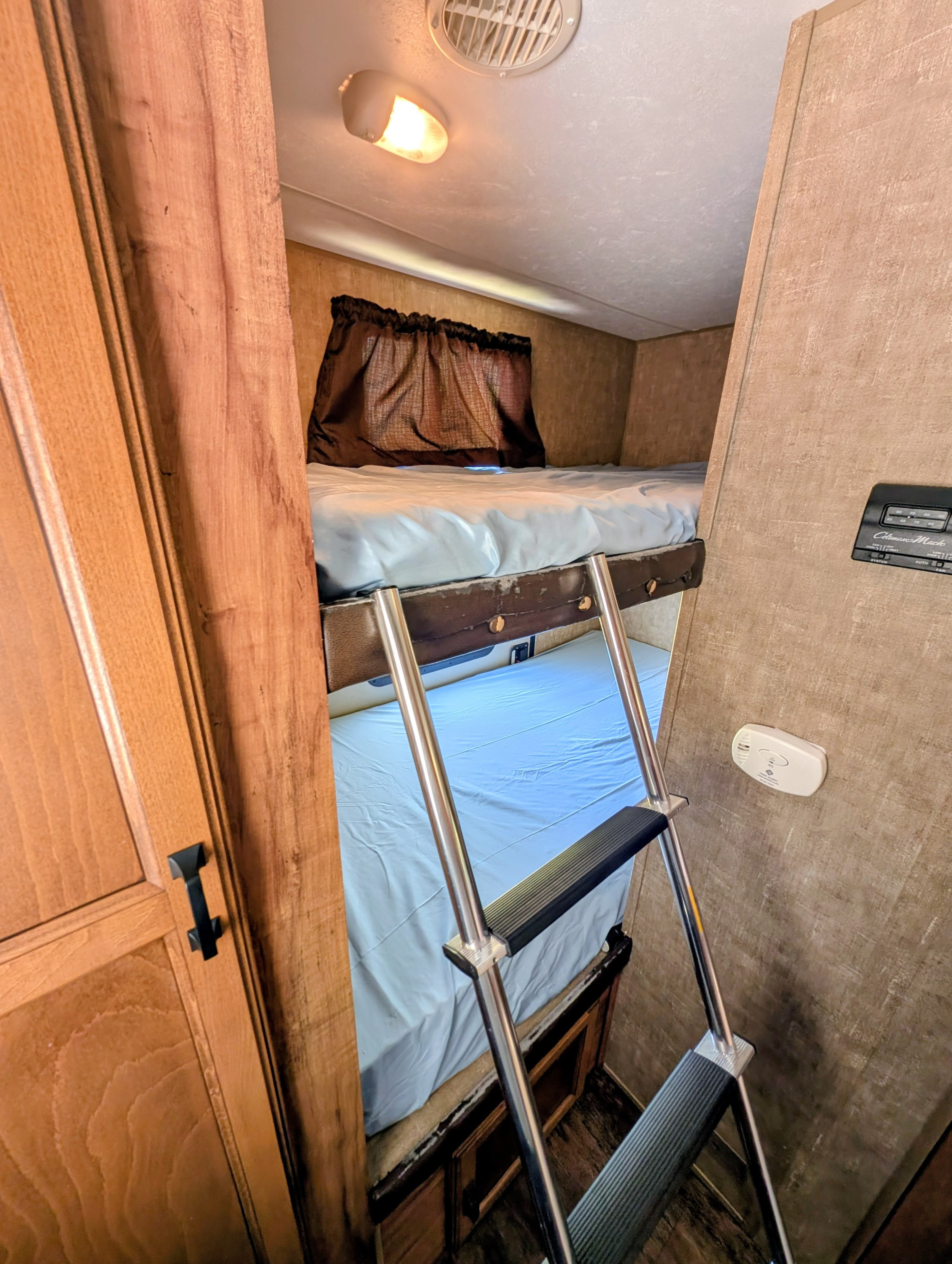 Interior of an **rv rental** showing cozy bunk beds with light blue sheets, a ladder, overhead lighting, and wood paneling.. KZ Spree Connect C231BHS 2015