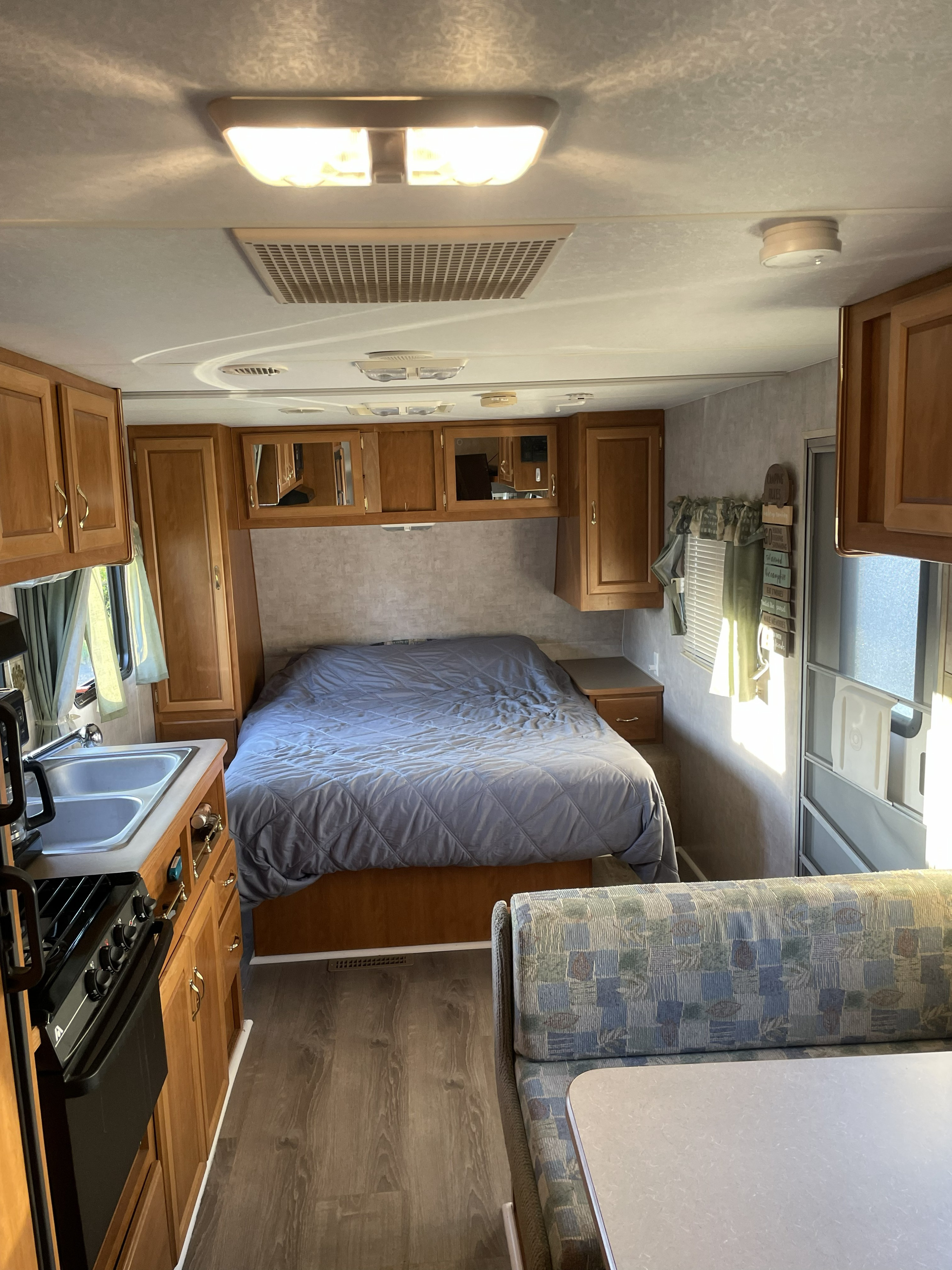 RV rental interior: bedroom with gray bed, a compact kitchen with sink/stove, and a dinette with patterned seats.. Fleetwood Mallard 2005