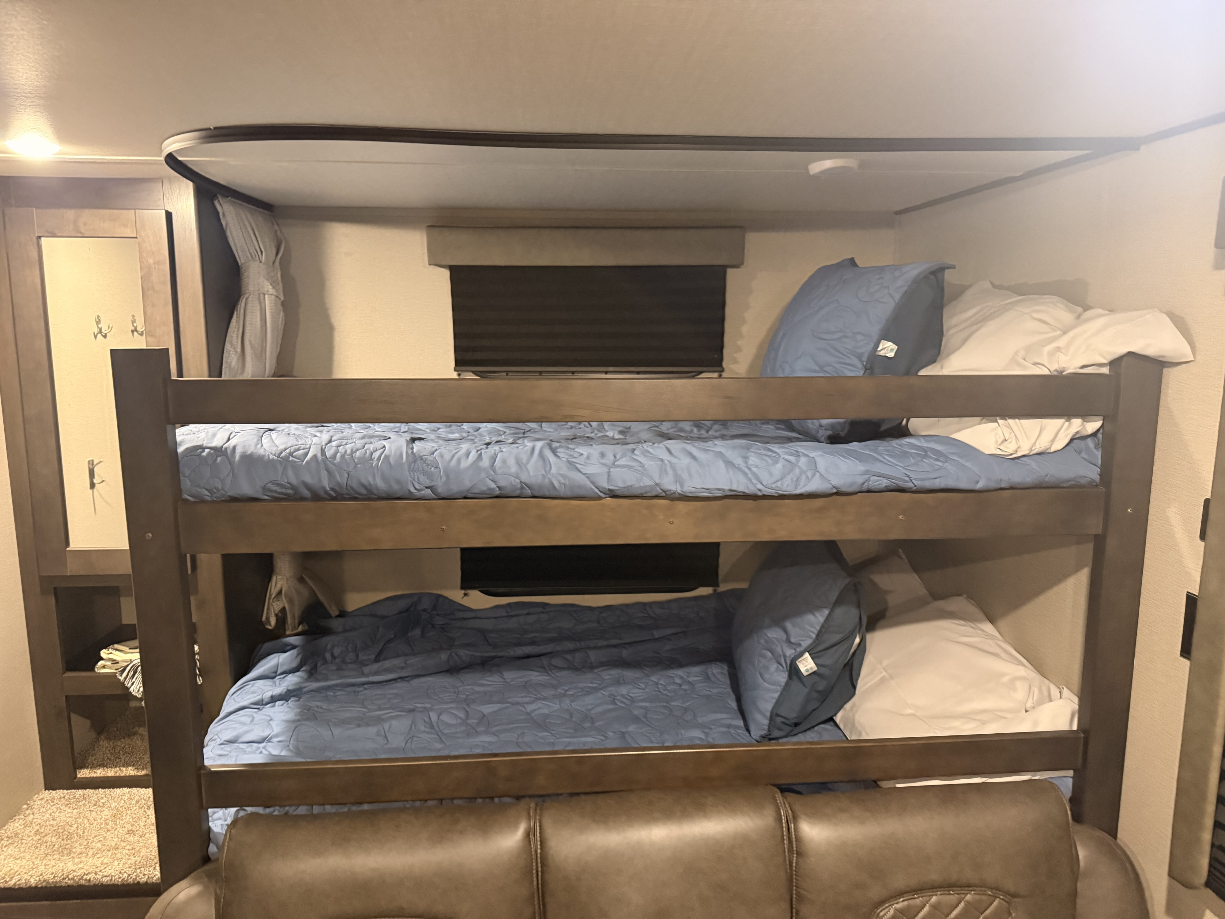 RV rental: This image showcases a cozy RV interior with two-tier bunk beds featuring blue bedding, positioned above a brown leather sofa.. Grand Design Transcend Xplor 2021