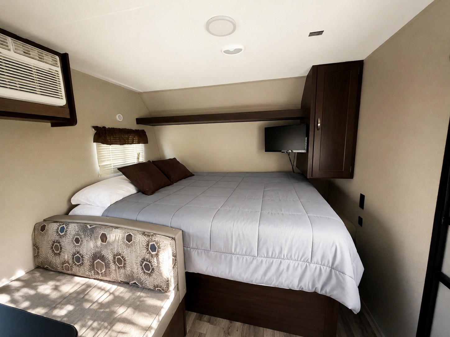 RV rental bedroom with a cozy bed, AC, wall-mounted TV, storage cabinet, and upholstered bench seating.. Keystone RV Summerland Mini 2018