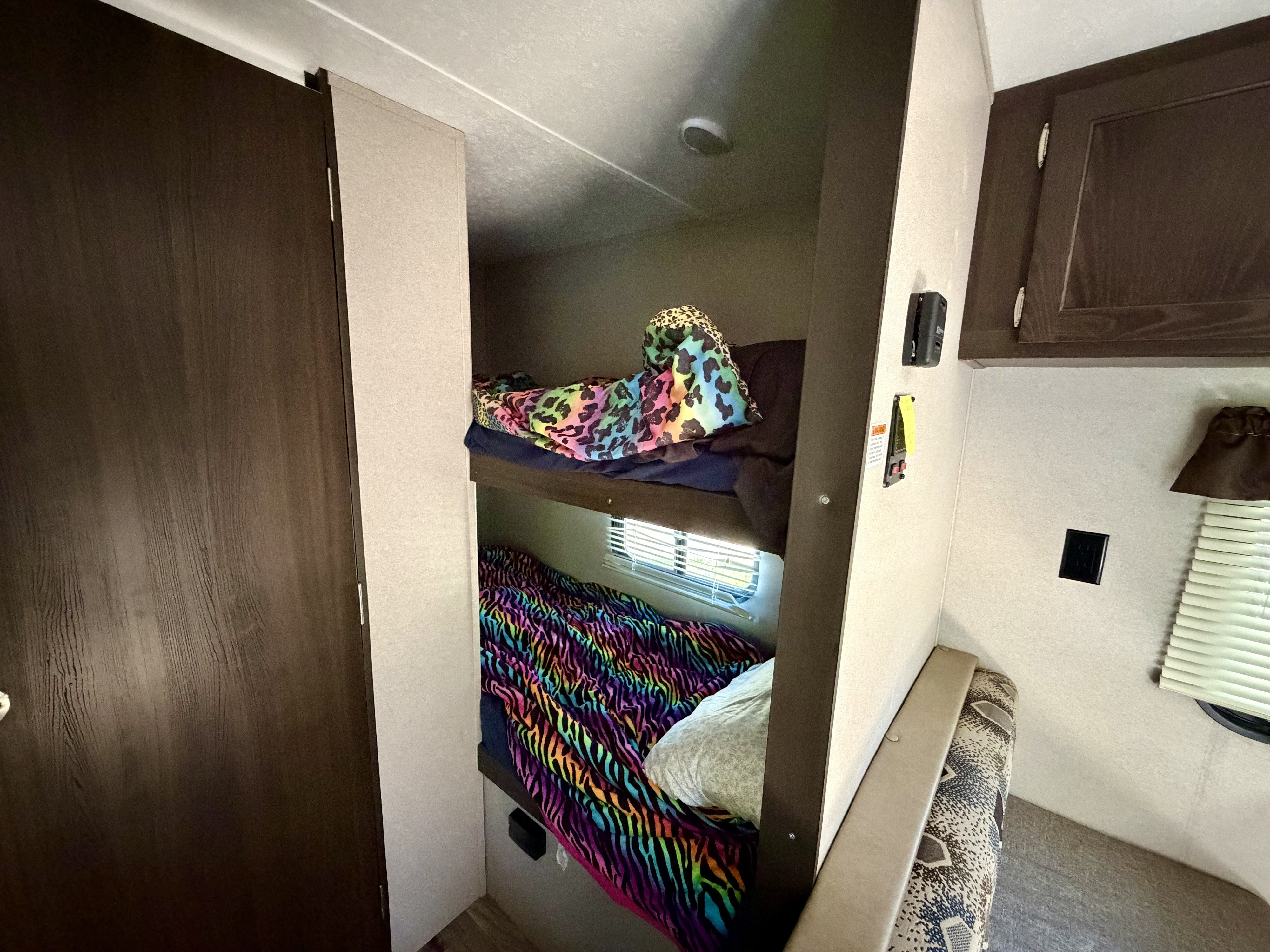 Cozy bunk beds inside an RV rental: vibrant blankets, a window, and a door on the left frame this compact sleeping area.. Keystone RV Summerland Mini 2018
