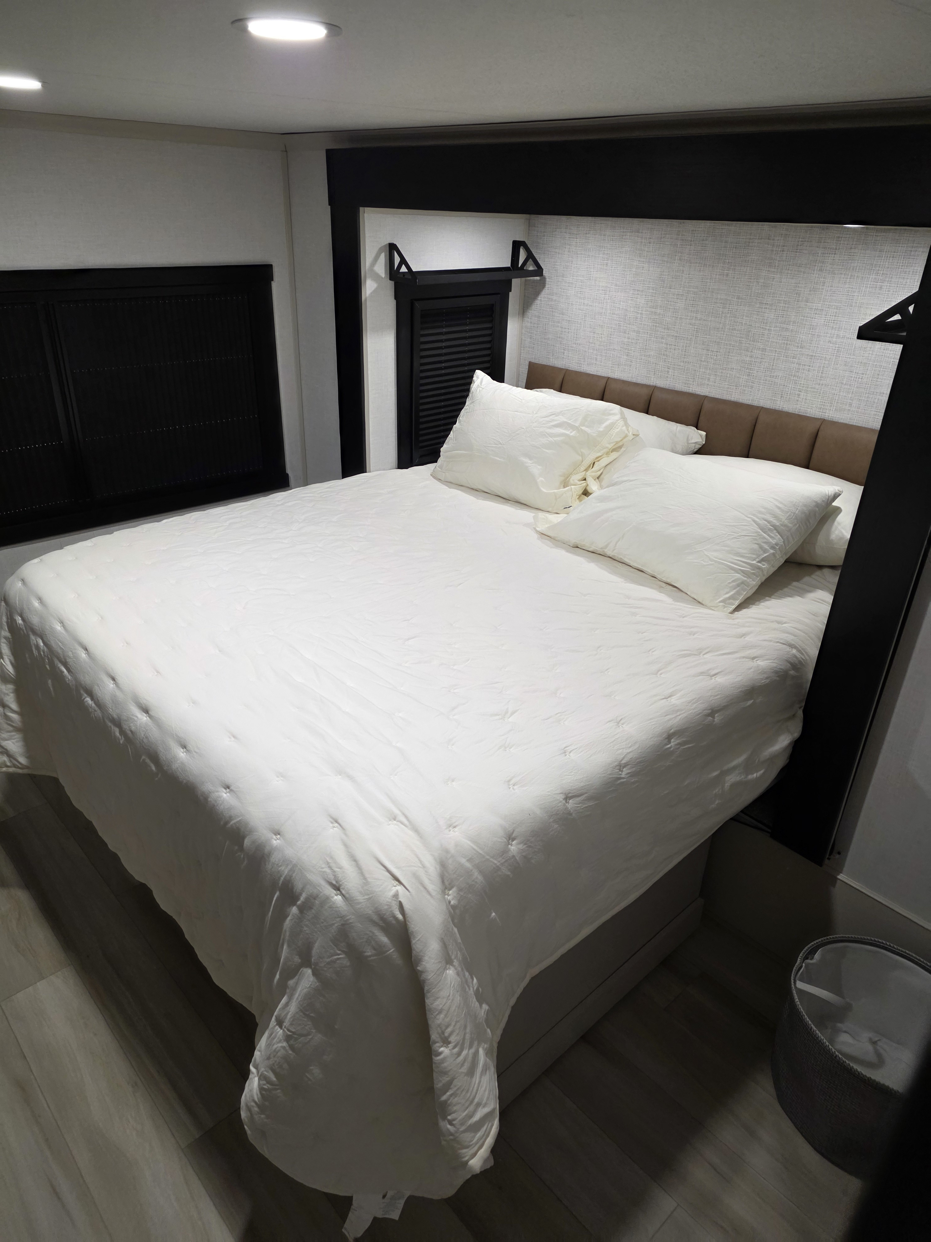 Modern RV rental bedroom with a neatly made bed, white bedding, soft pillows, a brown headboard, and dark trim.. Forest River Salem Hemisphere 2025