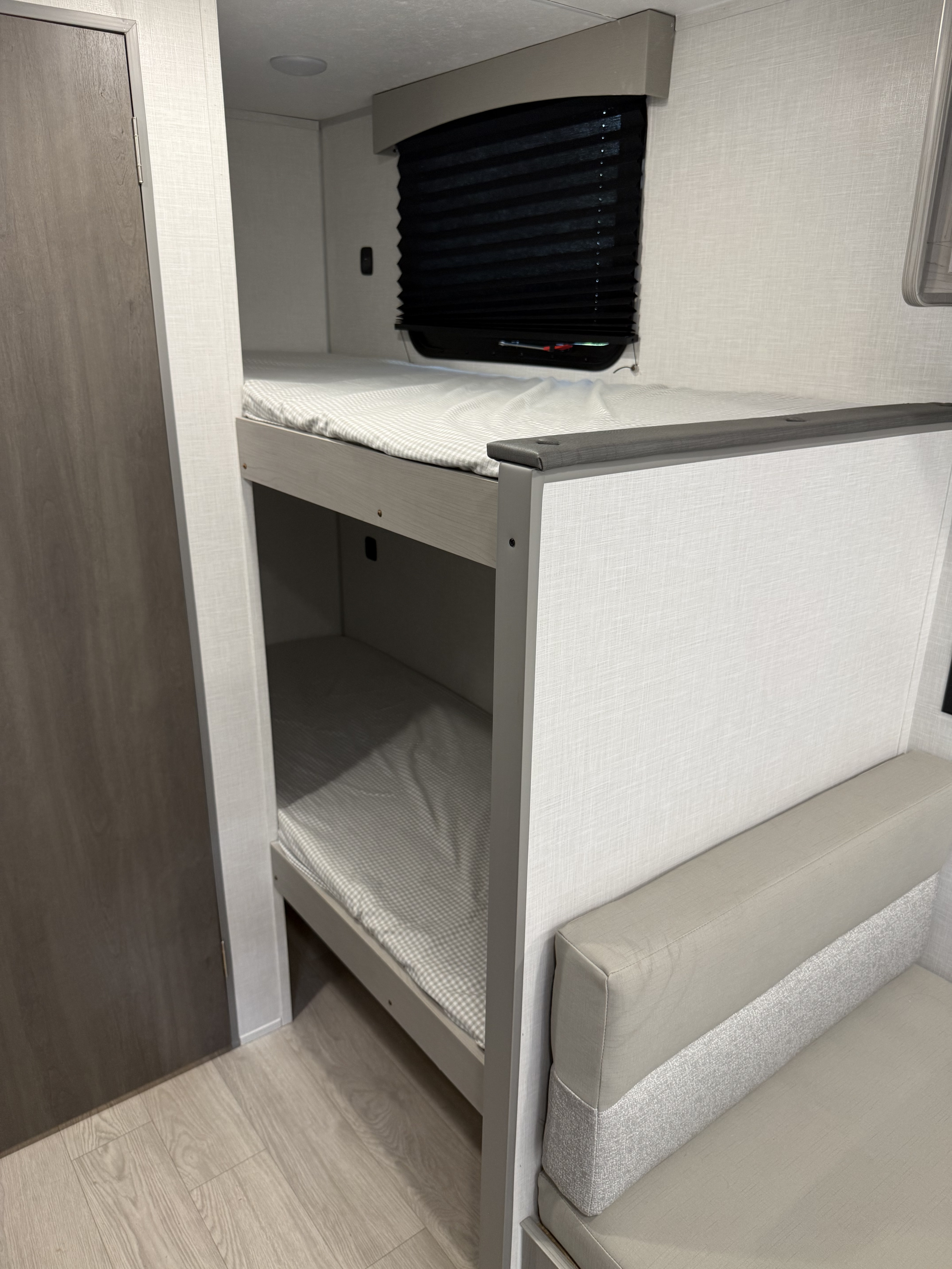 RV rental interior: two cozy bunk beds with checkered sheets, a window, and adjacent sofa seating. Perfect for family adventures.. Coachman Clipper 2026