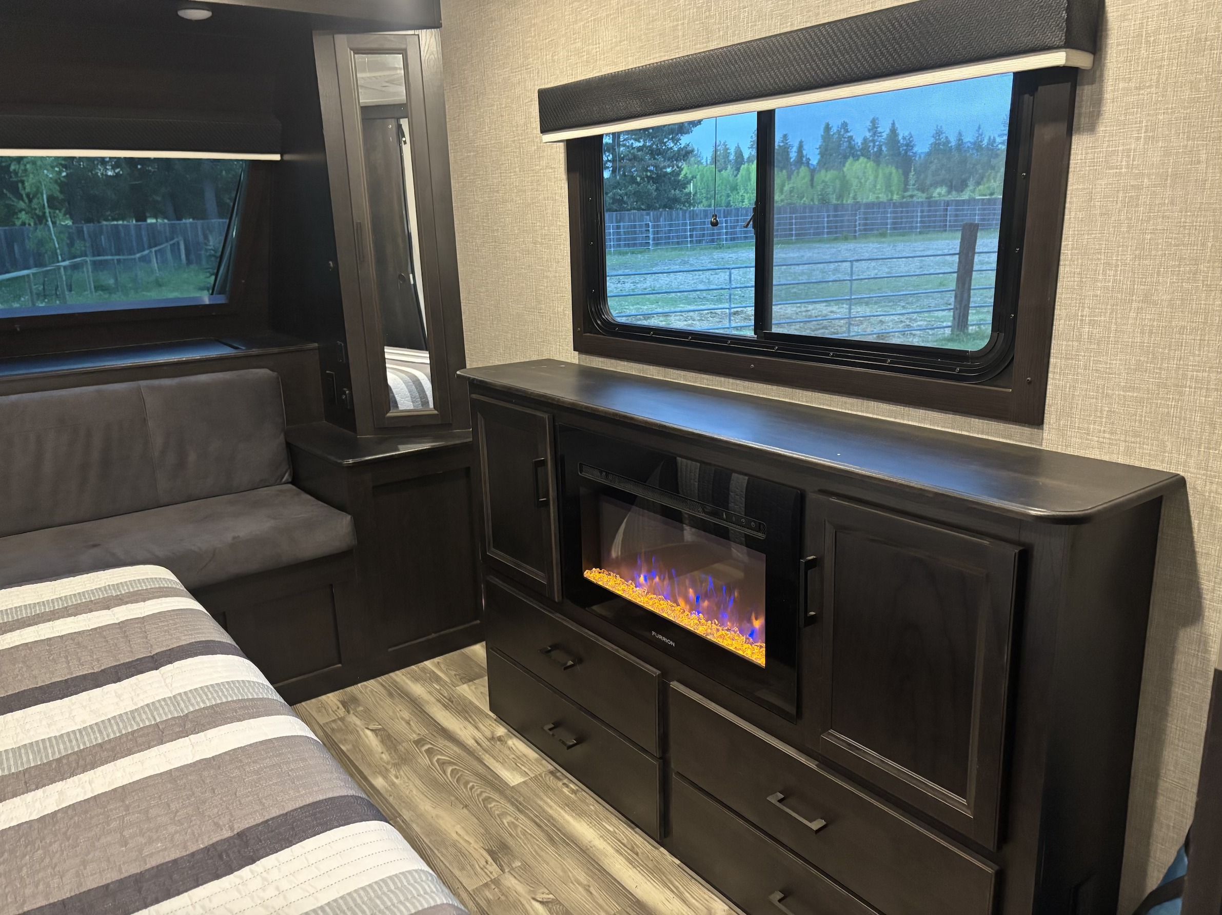 Cozy RV rental interior: bed, bench seating, electric fireplace, dark wood cabinetry, and scenic outdoor views.. Jayco Eagle HT 2023