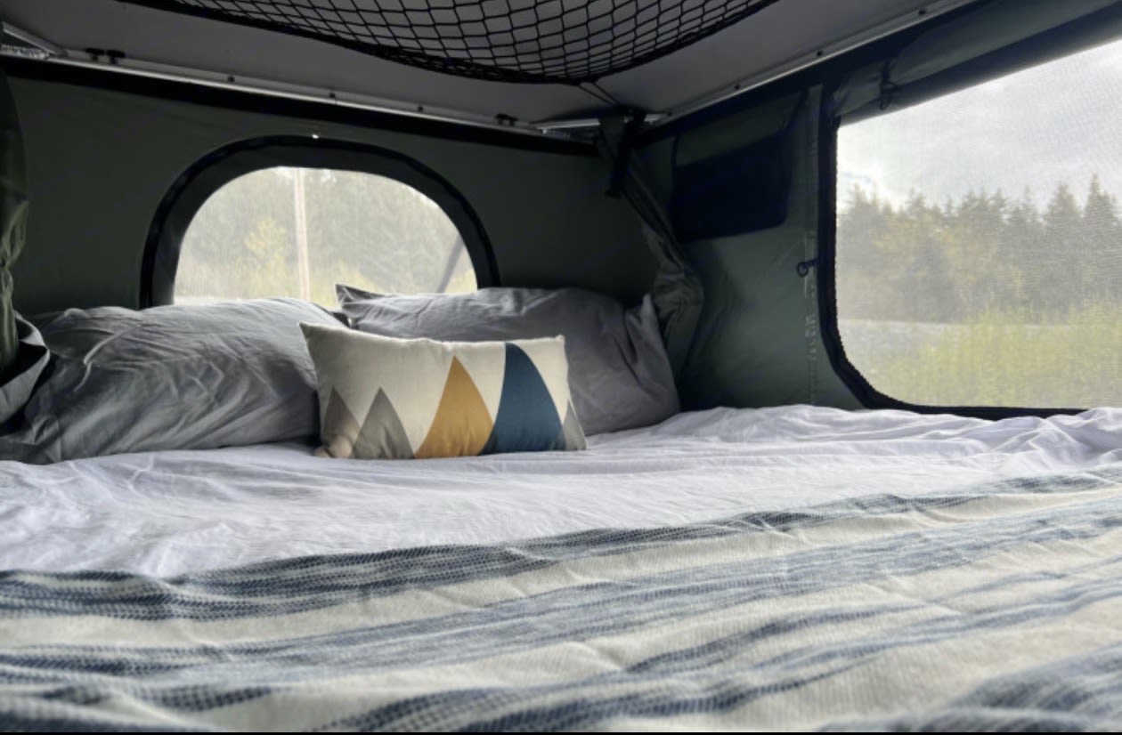 Cozy RV rental sleeping area: bed, pillows, & scenic window view of trees. Perfect for camping & outdoor adventures.. Toyota Tacoma 2013