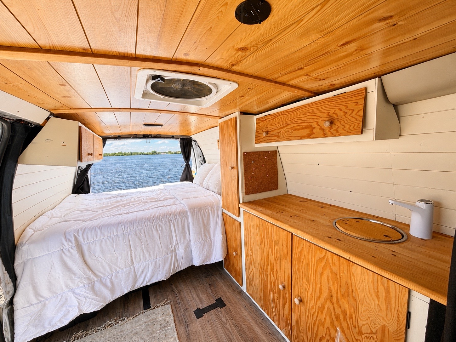 Cozy RV rental interior: a bed looking out to a lake, wooden kitchenette, and ceiling. Perfect for your next van life trip!. Chevrolet Express 2500 2009