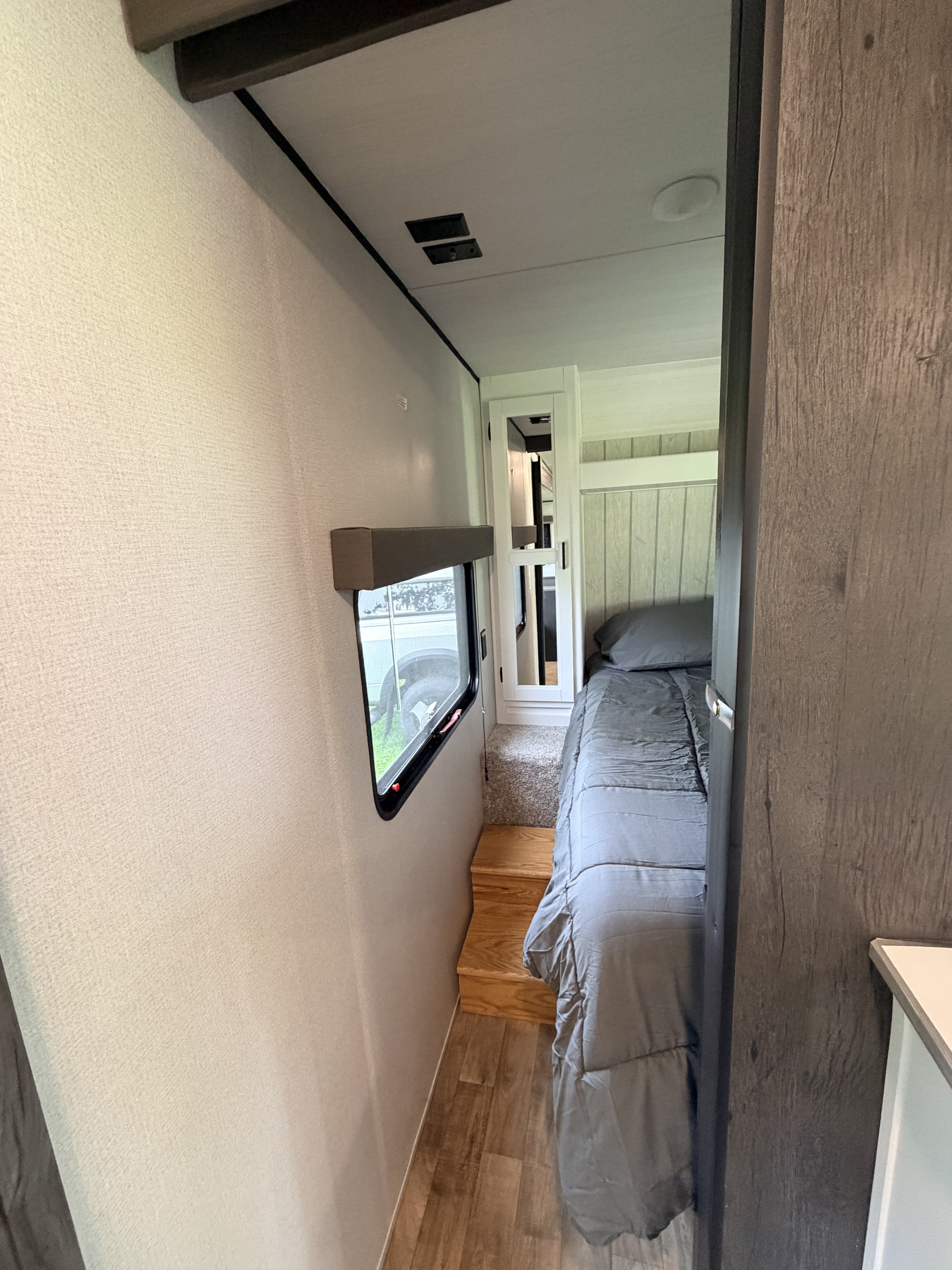 A cozy RV rental bedroom features a raised bed with grey bedding, accessible via wooden steps. Compact and functional.. Keystone RV Hideout 2022