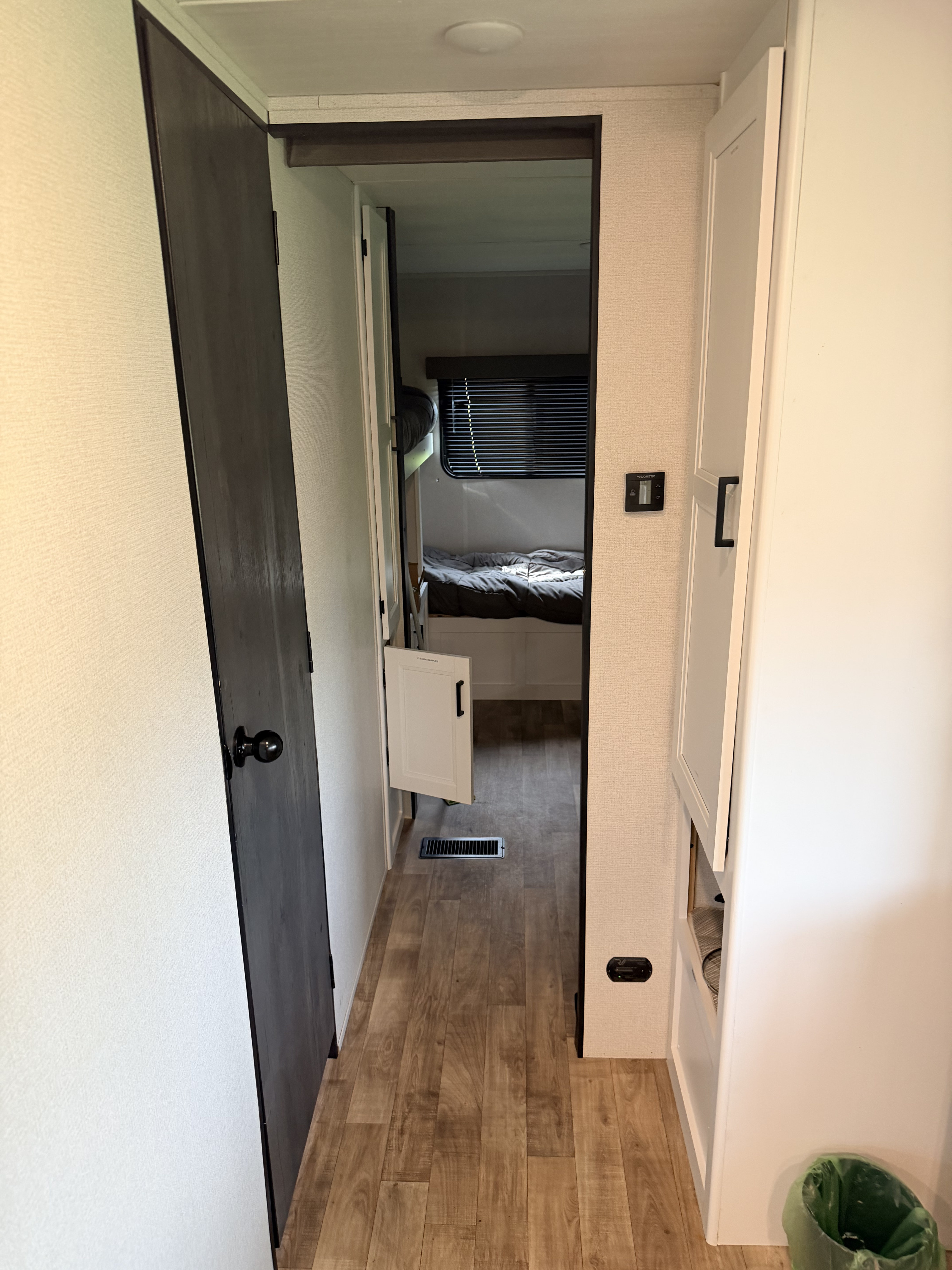 Inside an rv rental: a cozy hallway leads to a bedroom. Features include a thermostat, storage, and wood-look flooring.. Keystone RV Hideout 2022