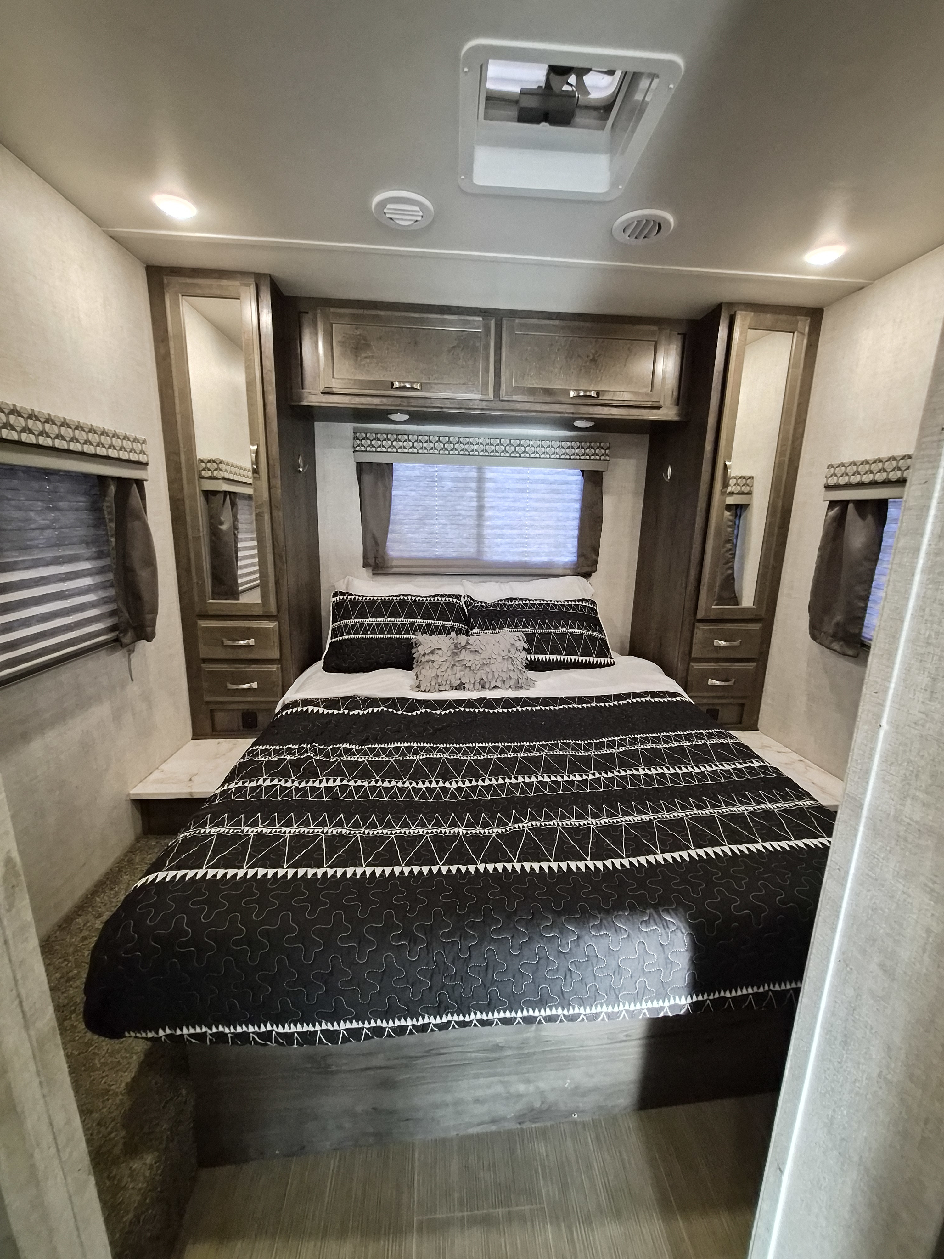 Cozy RV rental bedroom featuring patterned bedding, wood cabinets, mirrored storage, ceiling vents, and a skylight overhead.. Gulf Stream Conquest 2021