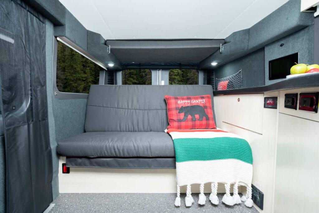 Experience comfort in this RV rental! Interior features a comfy bench, plaid pillow, blanket, and overhead bed/storage.. Pleasure-Way Pleasure-Way Class B 2022