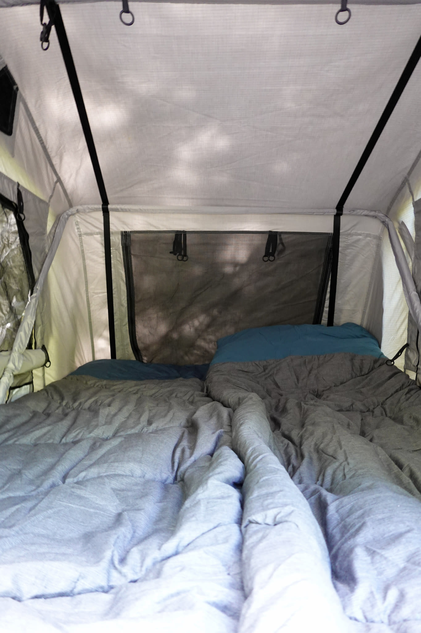 Interior of an RV rental rooftop tent showing a comfortable bed with grey and blue covers for camping.. Mazda Campervan 2008