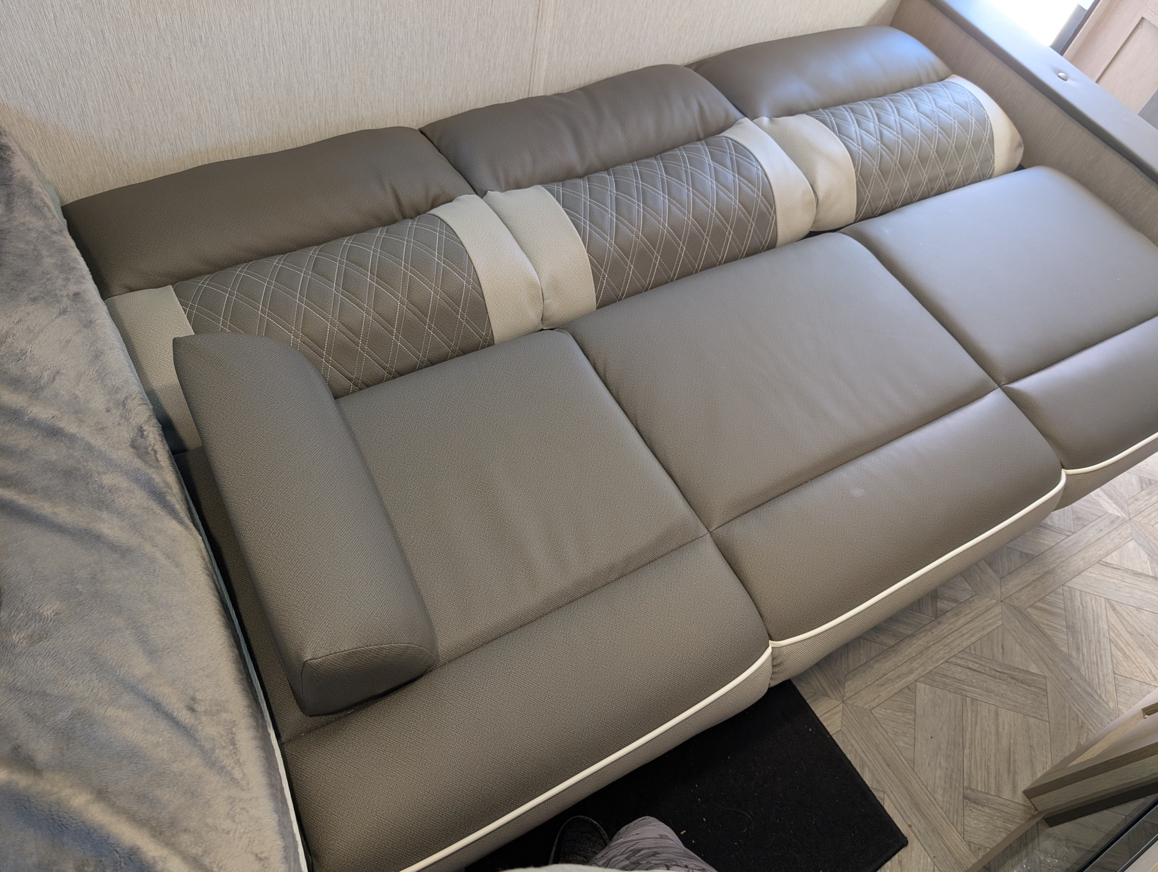 Comfortable gray sofa with quilted backrests in a modern rv rental interior, featuring white piping and a soft blanket.. Forest River Wildwood 2024