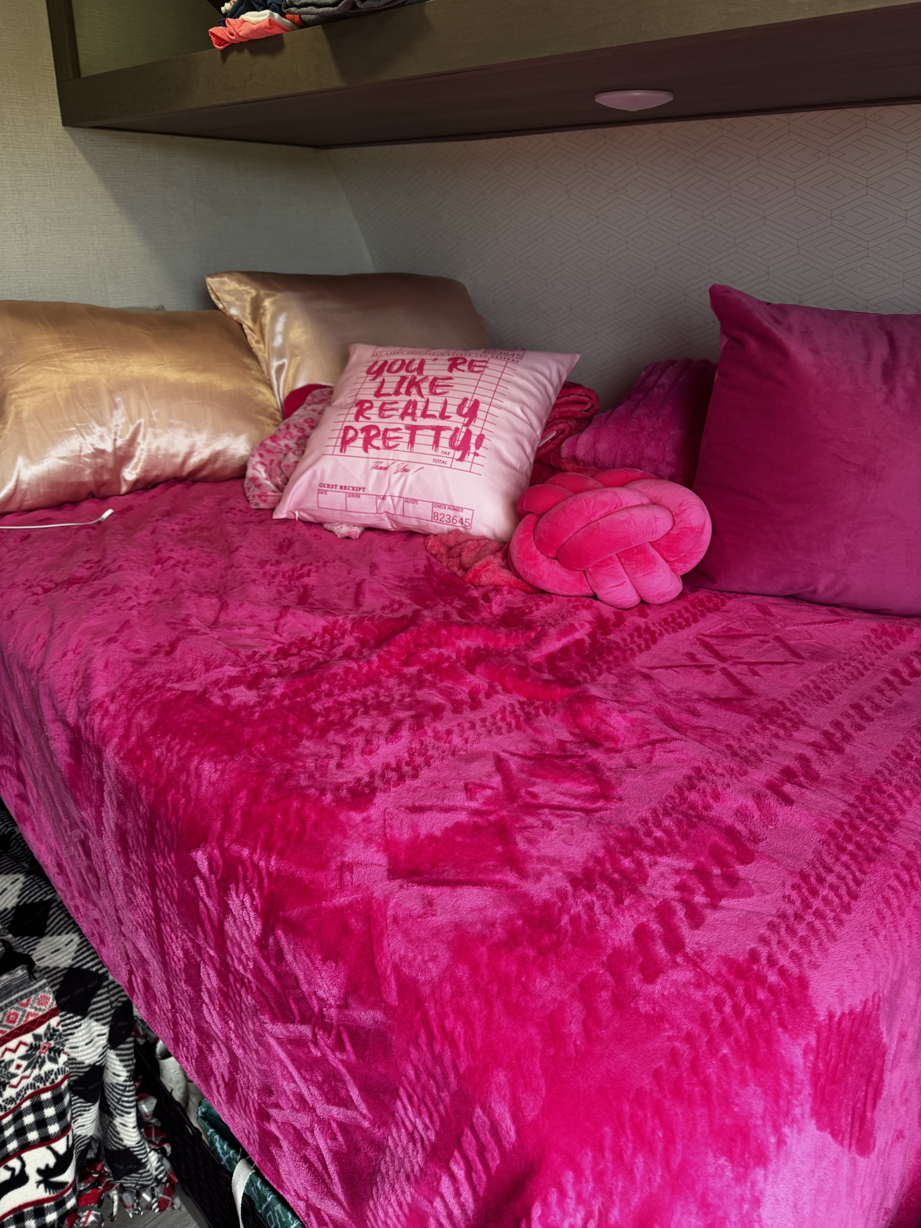 Cozy pink bunk in an rv rental with a fluffy hot pink blanket, satin pillows, and a pillow reading "YOU'RE REALLY PRETTY!".. Grand Design Transcend One 2025