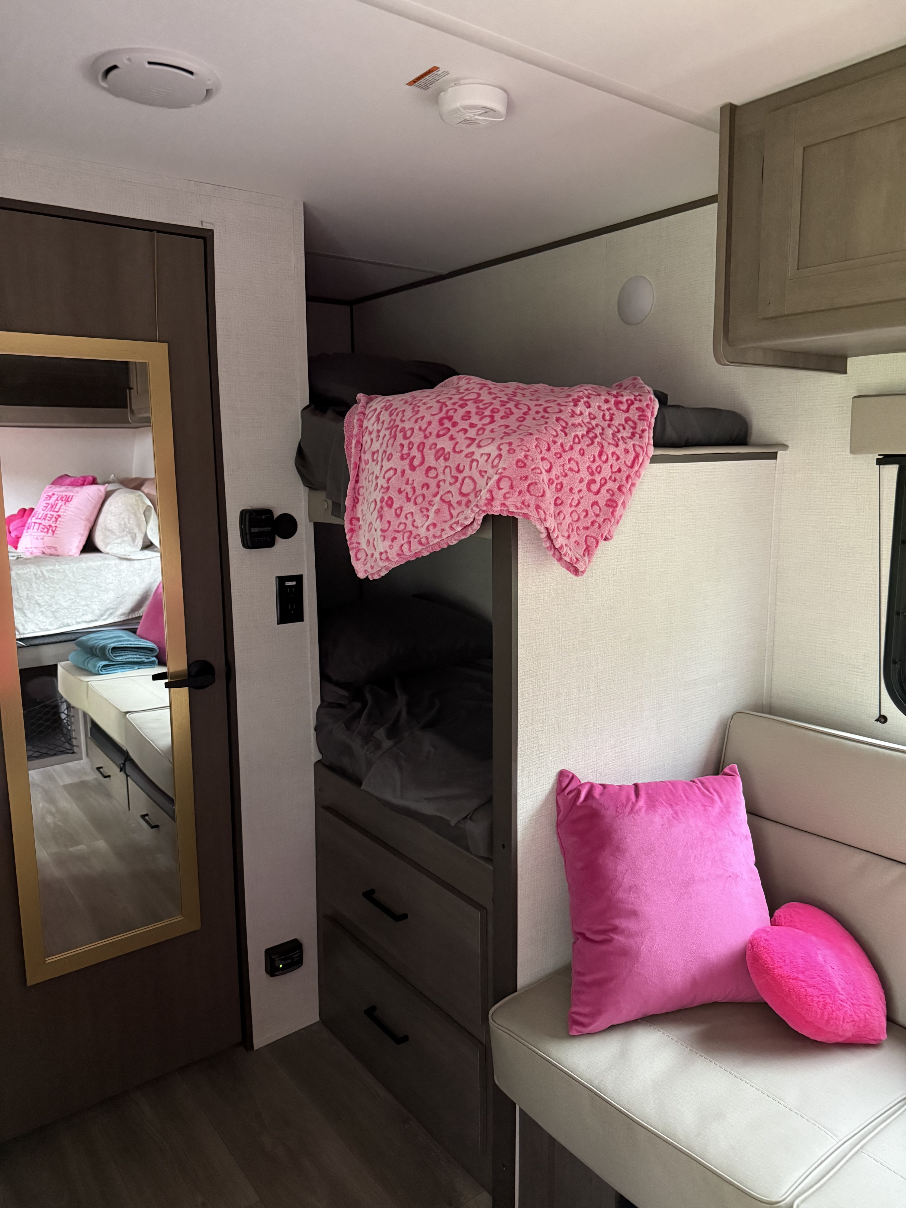Cozy rv rental interior featuring bunk beds, a comfy couch with pink pillows, and a mirrored door. Great for travel.. Grand Design Transcend One 2025