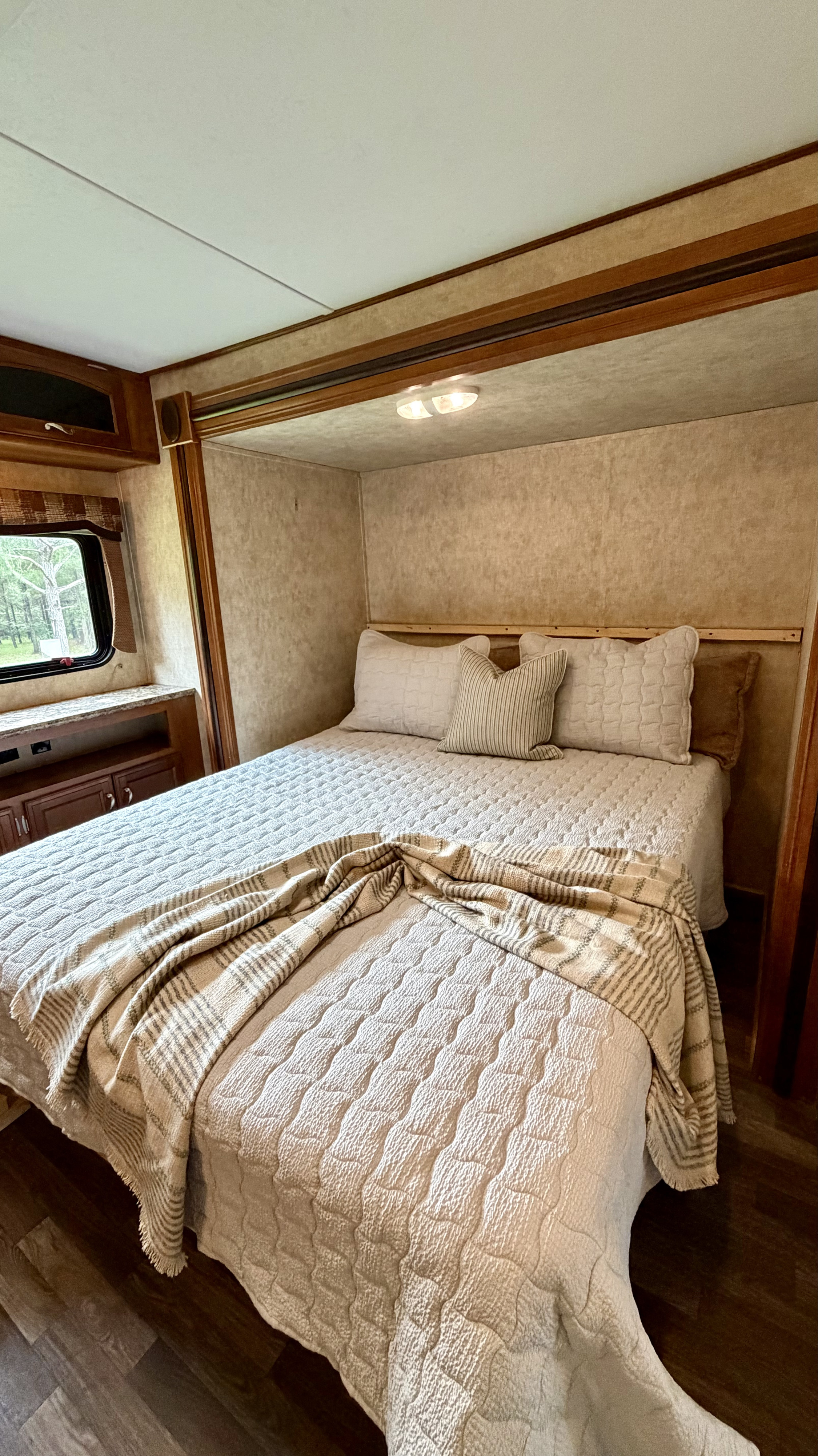 Cozy RV rental bedroom featuring a comfortable bed with light quilted bedding, pillows, and a window showcasing trees.. Avenger Avenger Trailer 2015