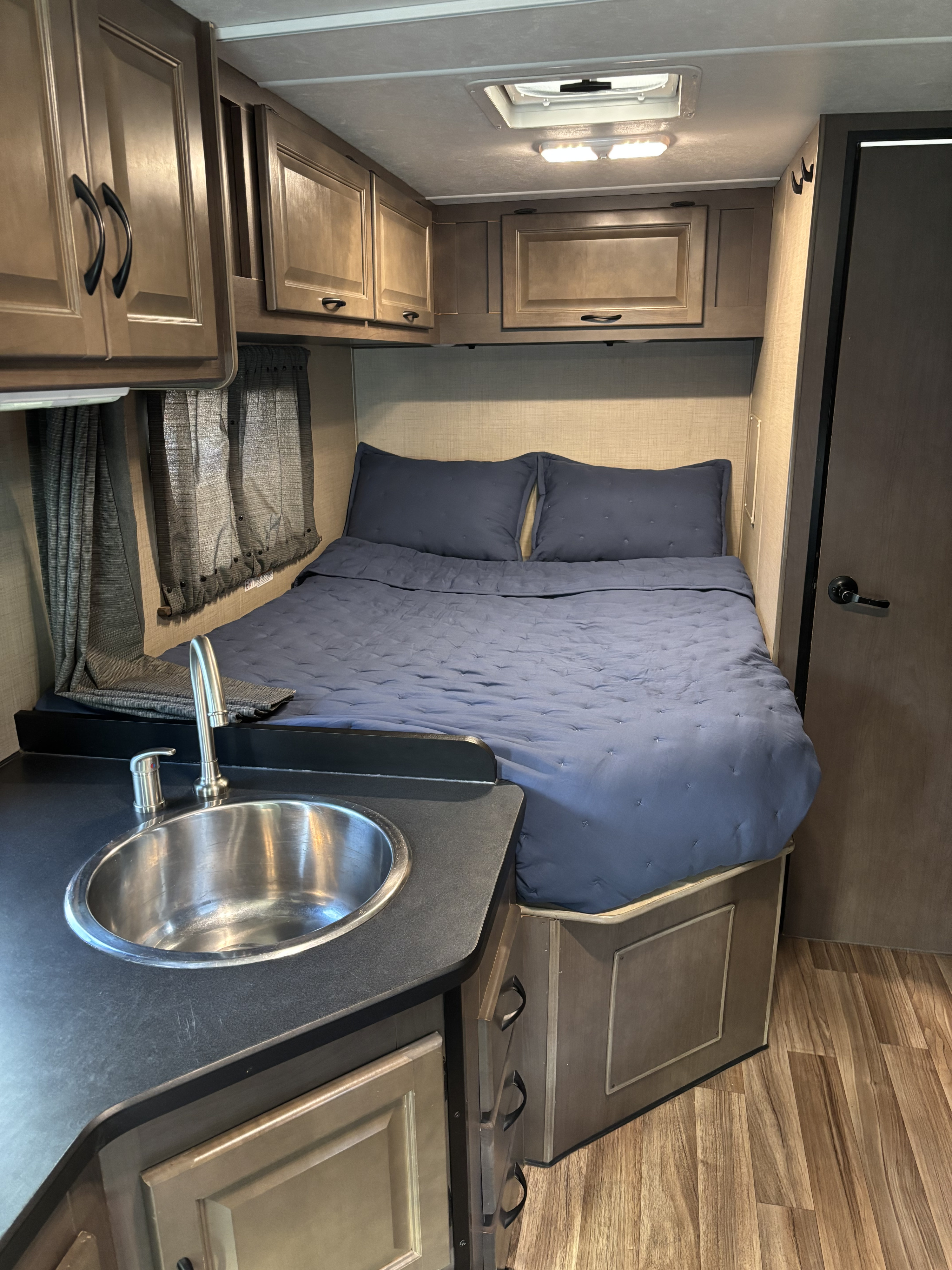 View inside a functional RV rental, featuring a compact bedroom with blue bedding, a small sink, and storage cabinets.. Thor Majestic 2020