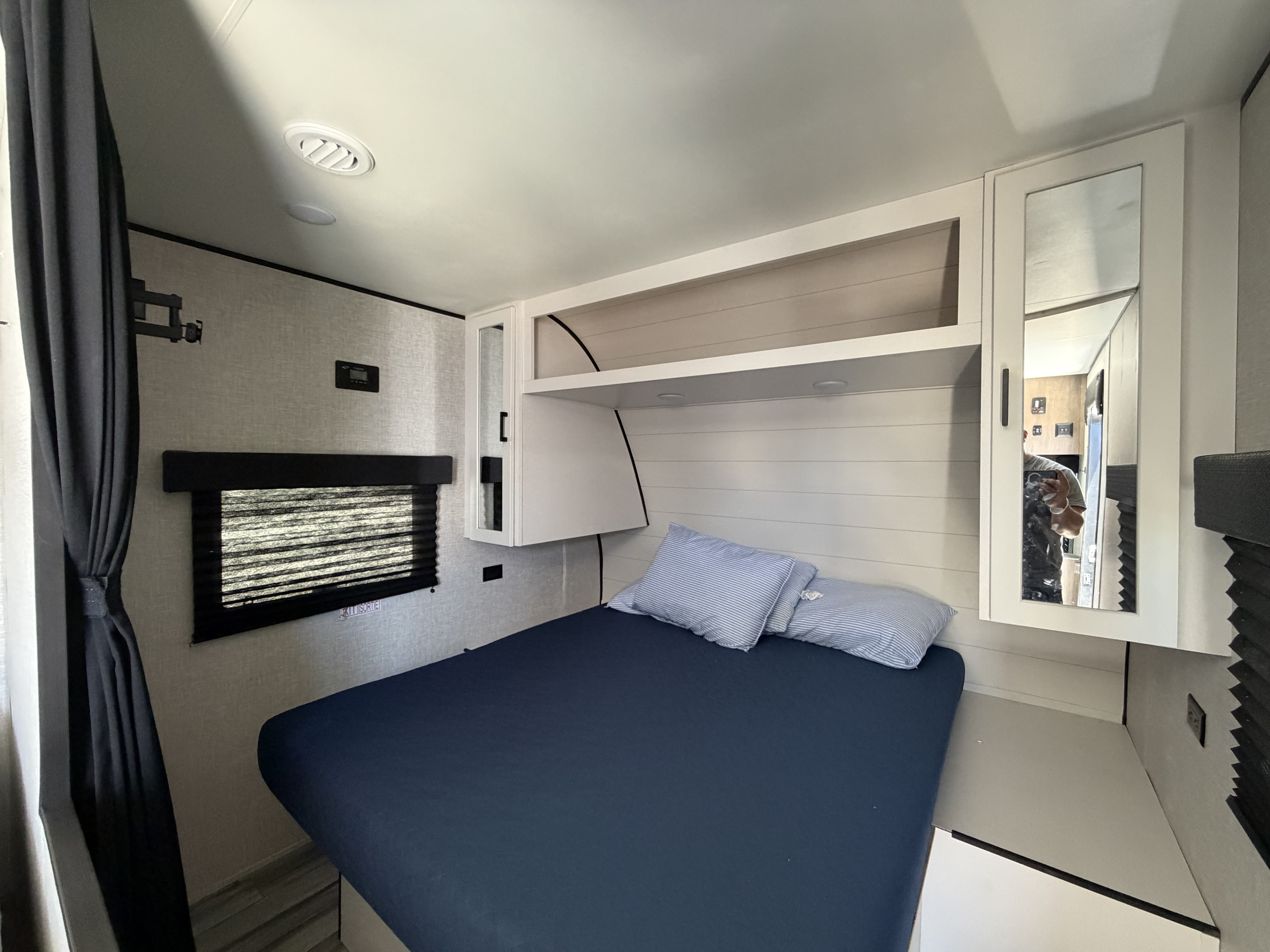 RV rental bedroom interior: blue bed, overhead storage, window, and mirrored cabinet for comfortable travel.. Jayco Jay Flight SLX 2025