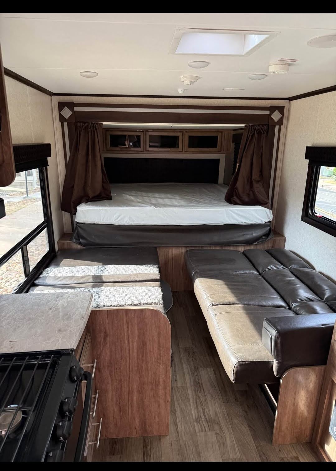 View inside an RV rental showing the bed, dinette, sofa, and a kitchen counter with stove in the foreground.. Jayco Jay Feather 2019
