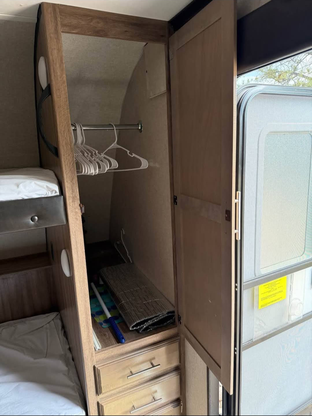 This RV rental interior features a cozy bunk bed next to an open closet with hangers, lower drawers, and an open exit door.. Jayco Jay Feather 2019