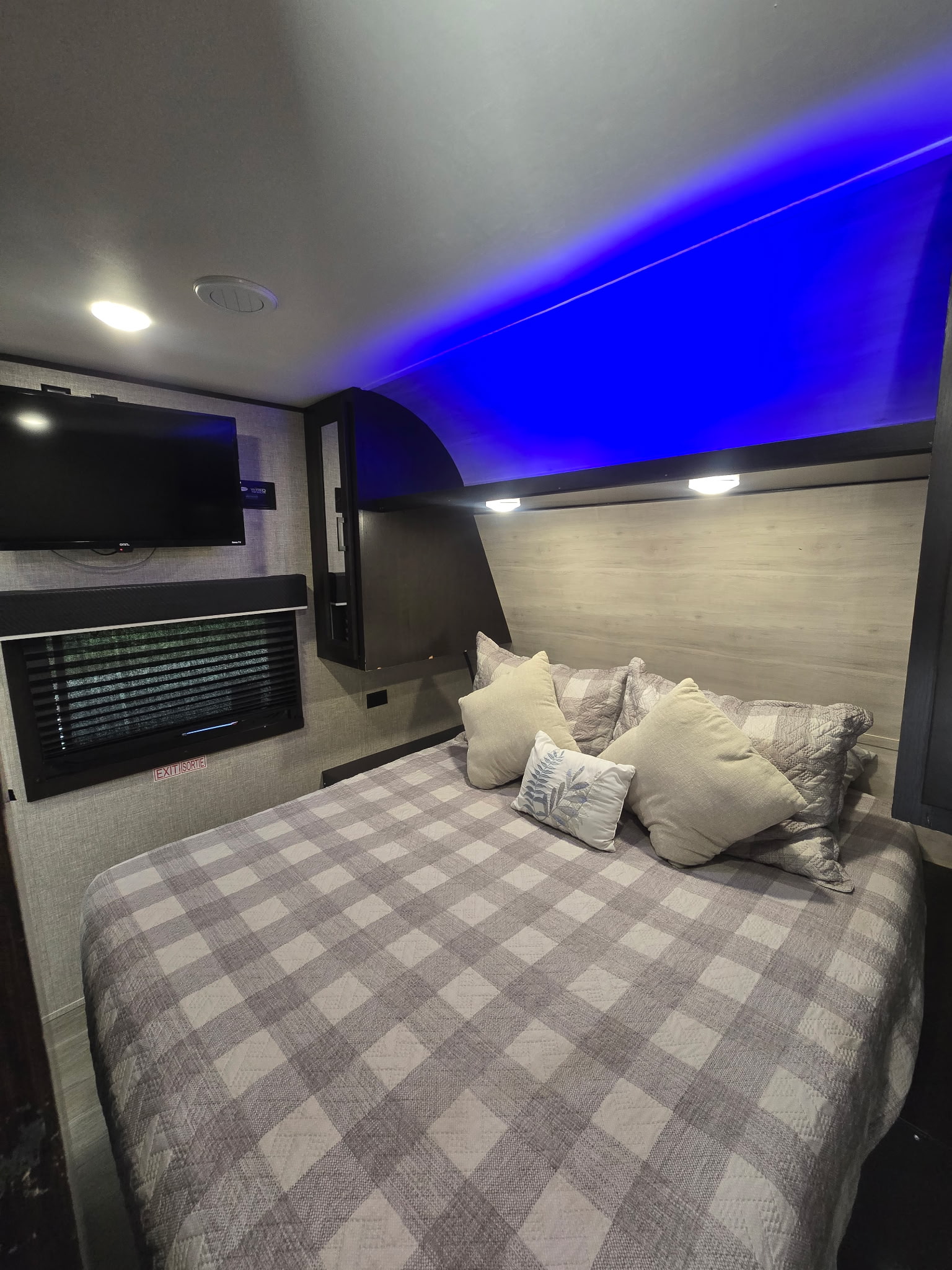 This RV rental features a comfortable bedroom with a checkered bedspread, mounted TV, and stylish blue accent lighting overhead.. Jayco Jay Flight SLX Rocky Mountain Edition 2022