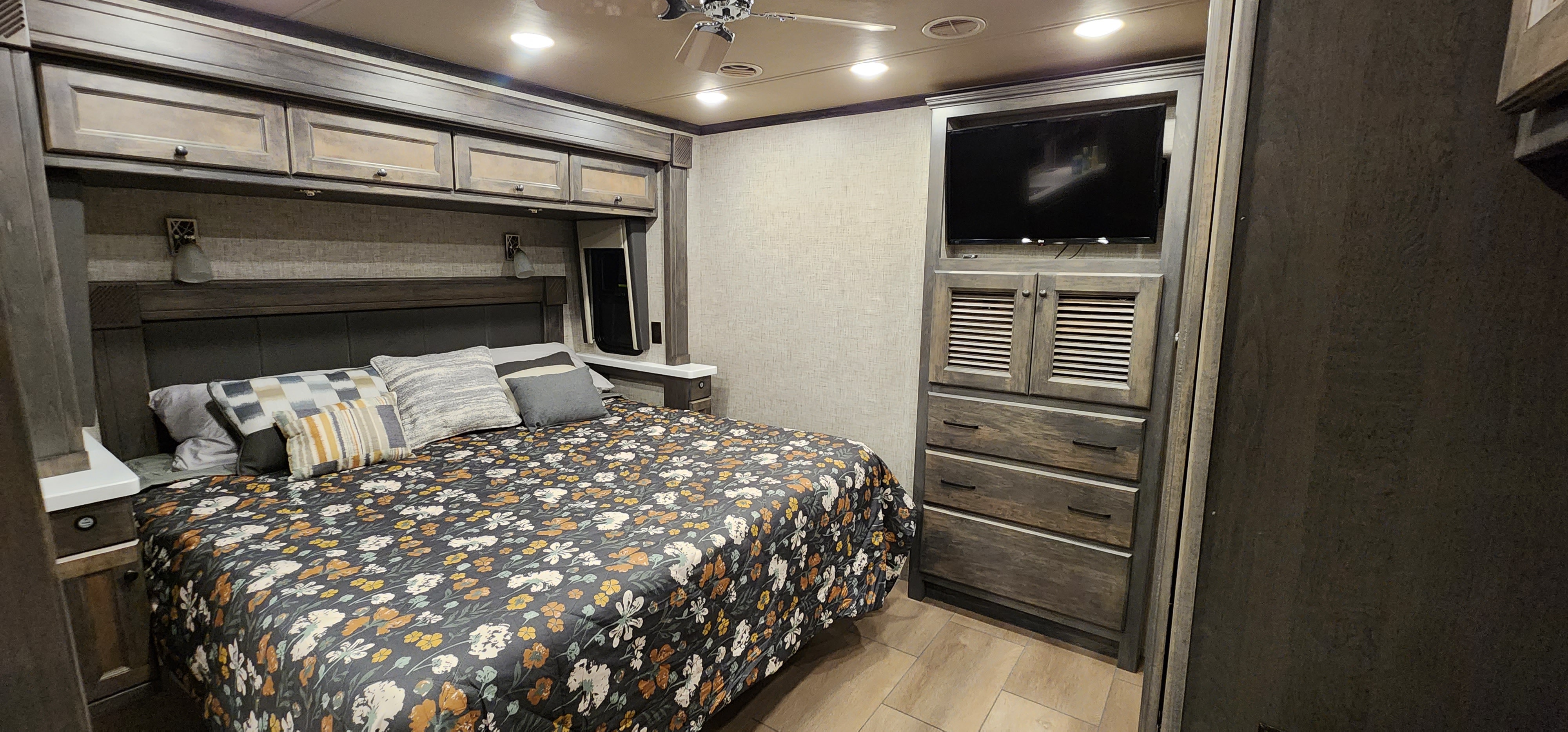 Comfortable RV rental bedroom featuring a floral bed, overhead cabinets, TV, and built-in storage for a cozy travel experience.. Allegro Allegro Open Road 2023