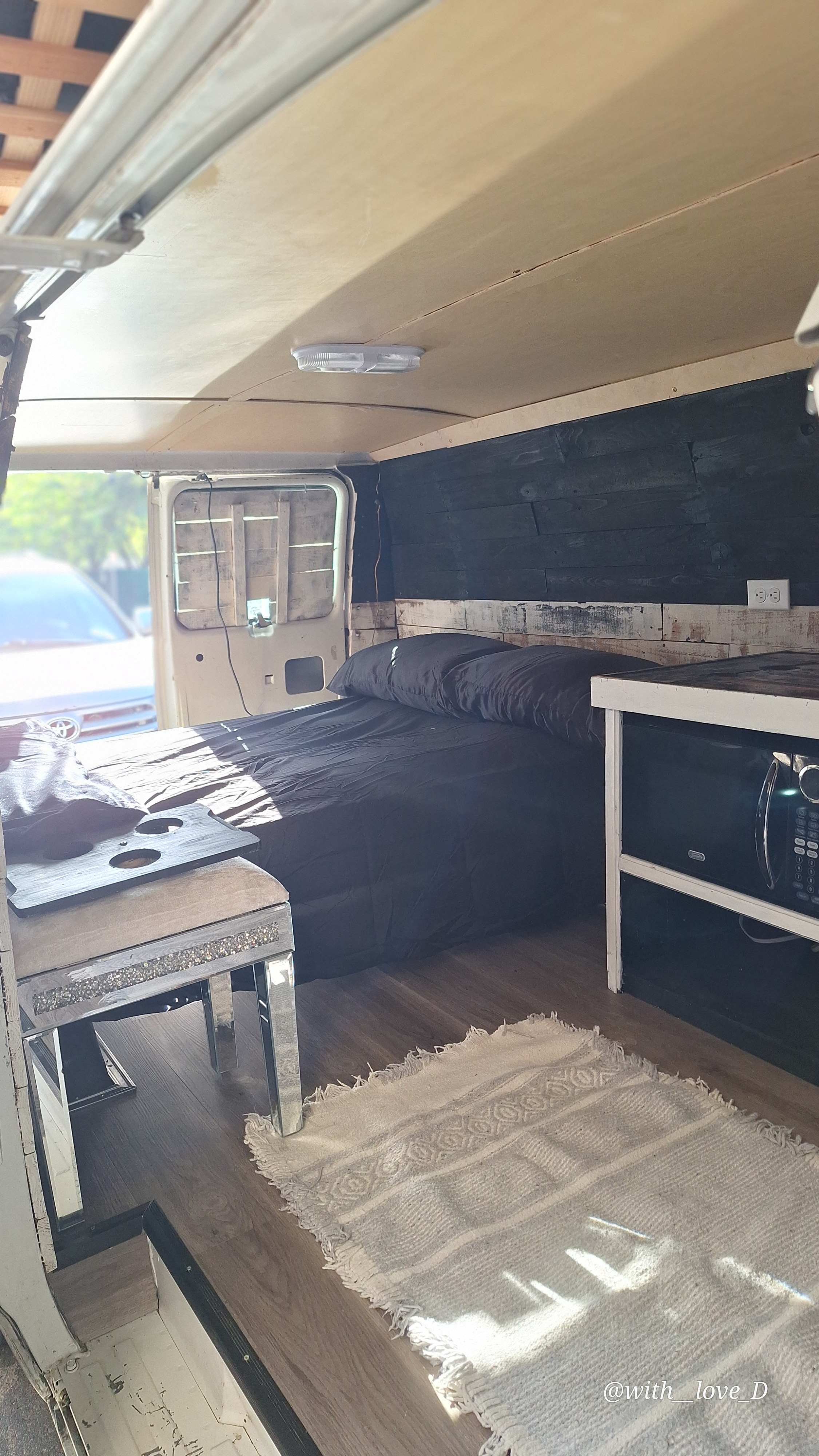 Step into this cozy RV rental interior: bed, microwave, wood walls, and laminate floor. Your van conversion adventure awaits!. Chevrolet G- Series 1995