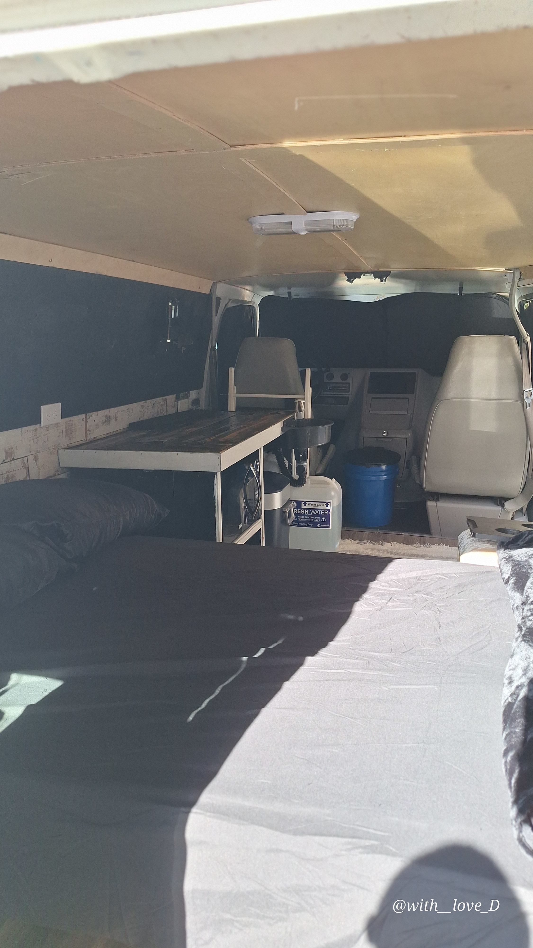Inside this customized RV rental: a comfortable bed, functional table, and mini kitchen/storage for van life.. Chevrolet G- Series 1995
