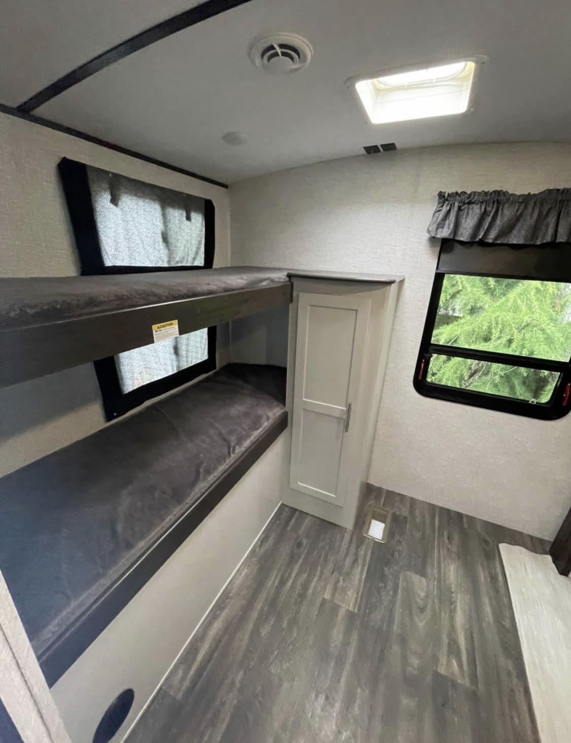 RV rental interior with comfortable bunk beds, a small wardrobe, and windows, showcasing a practical sleeping area.. Keystone RV Bullet Premier Ultra 2021