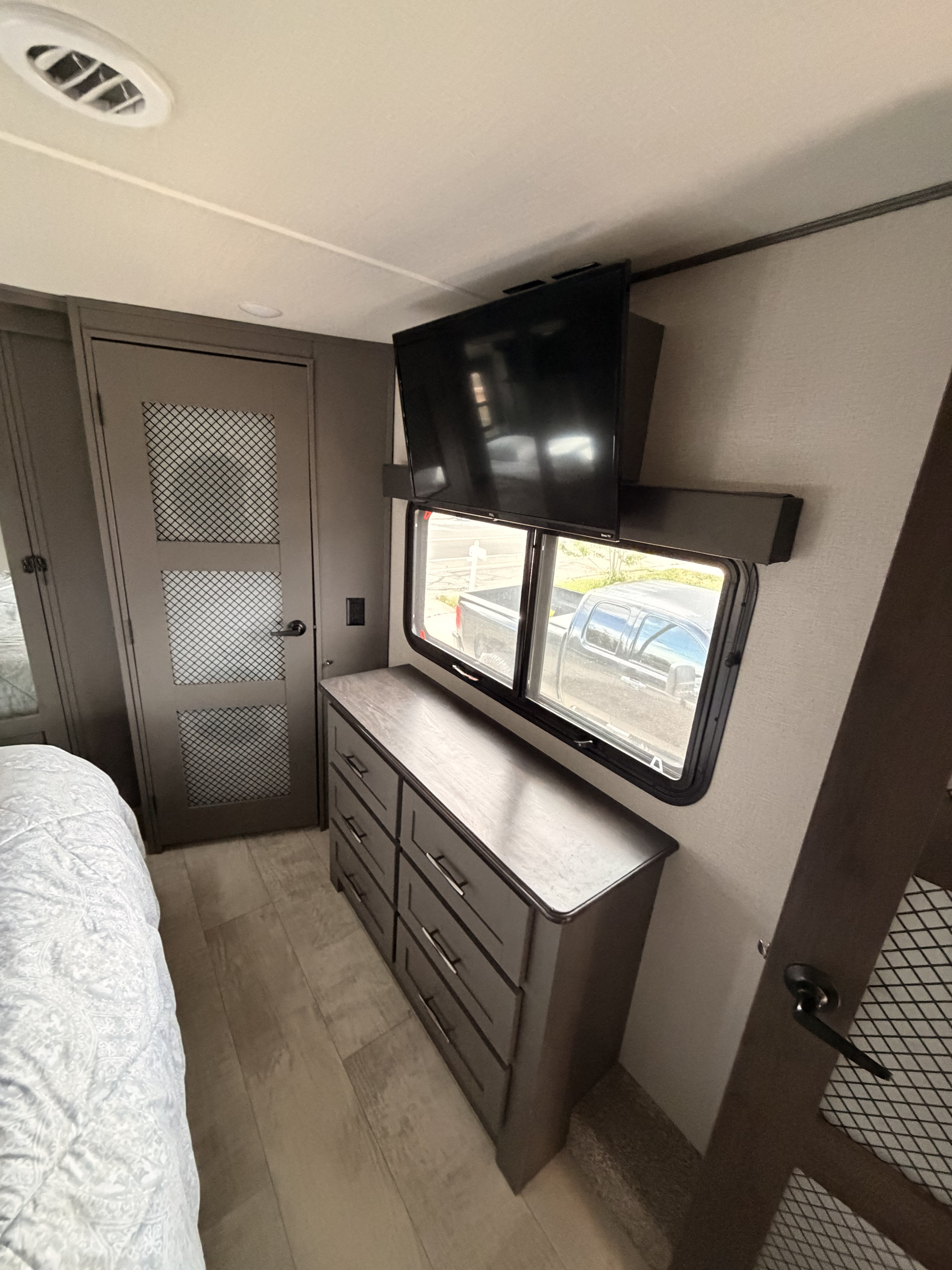 RV rental bedroom interior: modern dresser, mounted TV over window, stylish door, and comfy bed visible.. Grand Design Momentum Toy Hauler 2021