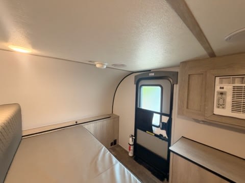 RV rental interior featuring a comfortable bed, wall AC unit, and entrance door, ready for your next adventure.. Riverside 511 2025