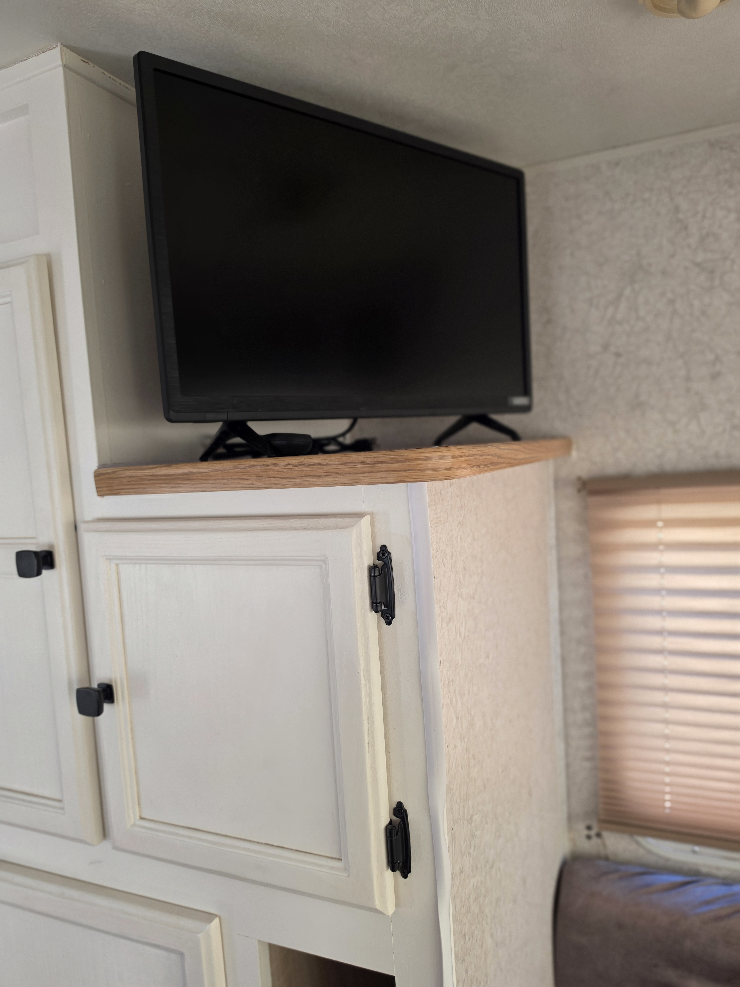 Modern RV rental interior with a TV on a wooden shelf above white cabinets, by a window.. R-Vision Trail-Lite Bantam 2002