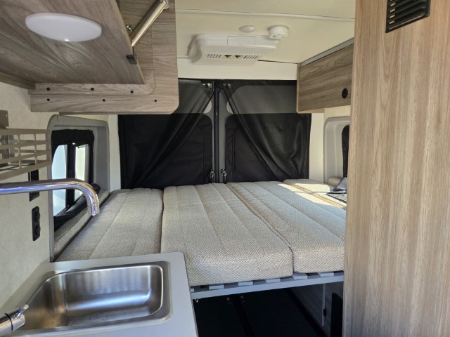 Inside an rv rental camper van: a cozy bed, kitchen sink, and overhead storage. Ideal for compact adventures.. Winnebago Solis 2023