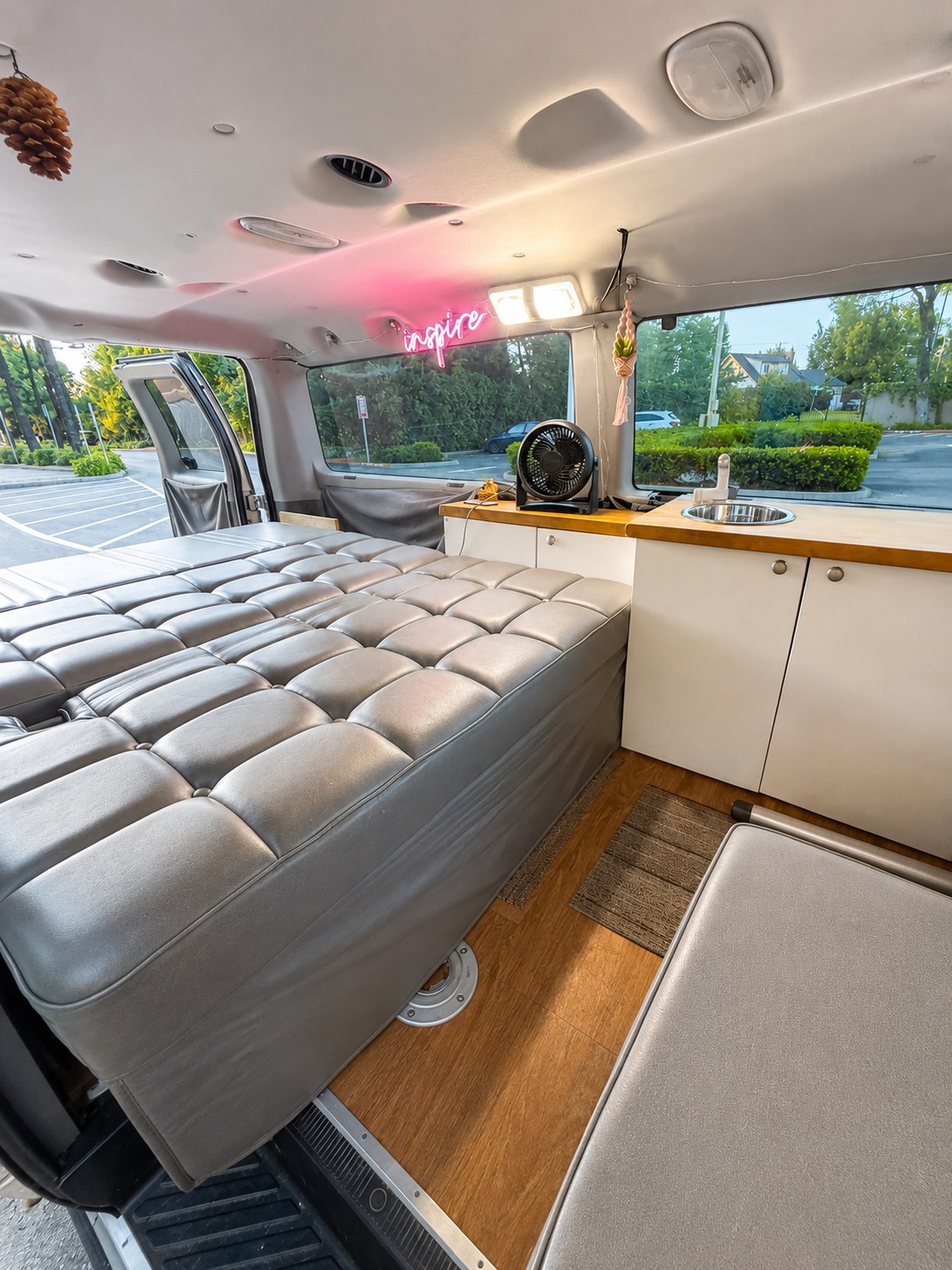 Cozy RV rental interior features a large gray bed, compact kitchenette with sink, and a bright 'inspire' neon sign.. Ford Econoline 2009
