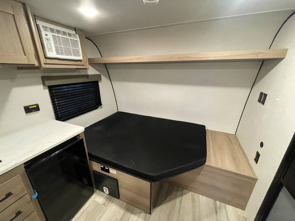 Cozy RV rental interior with a comfortable bed, AC unit, window, and kitchenette featuring an under-counter fridge.. Keystone RV Coleman 2026