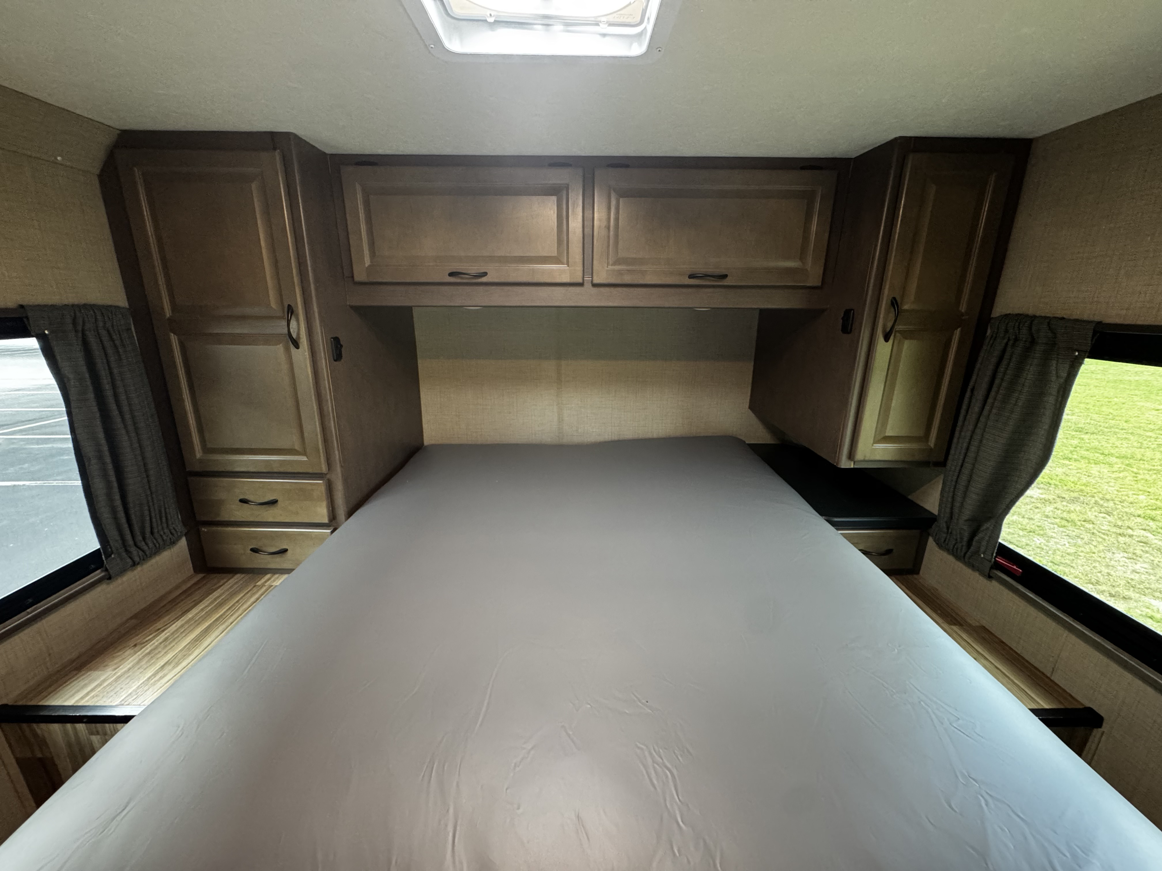 Cozy RV rental bedroom with a bed, wood-toned cabinets, side drawers, and windows with outdoor views.. Thor Majestic 2020