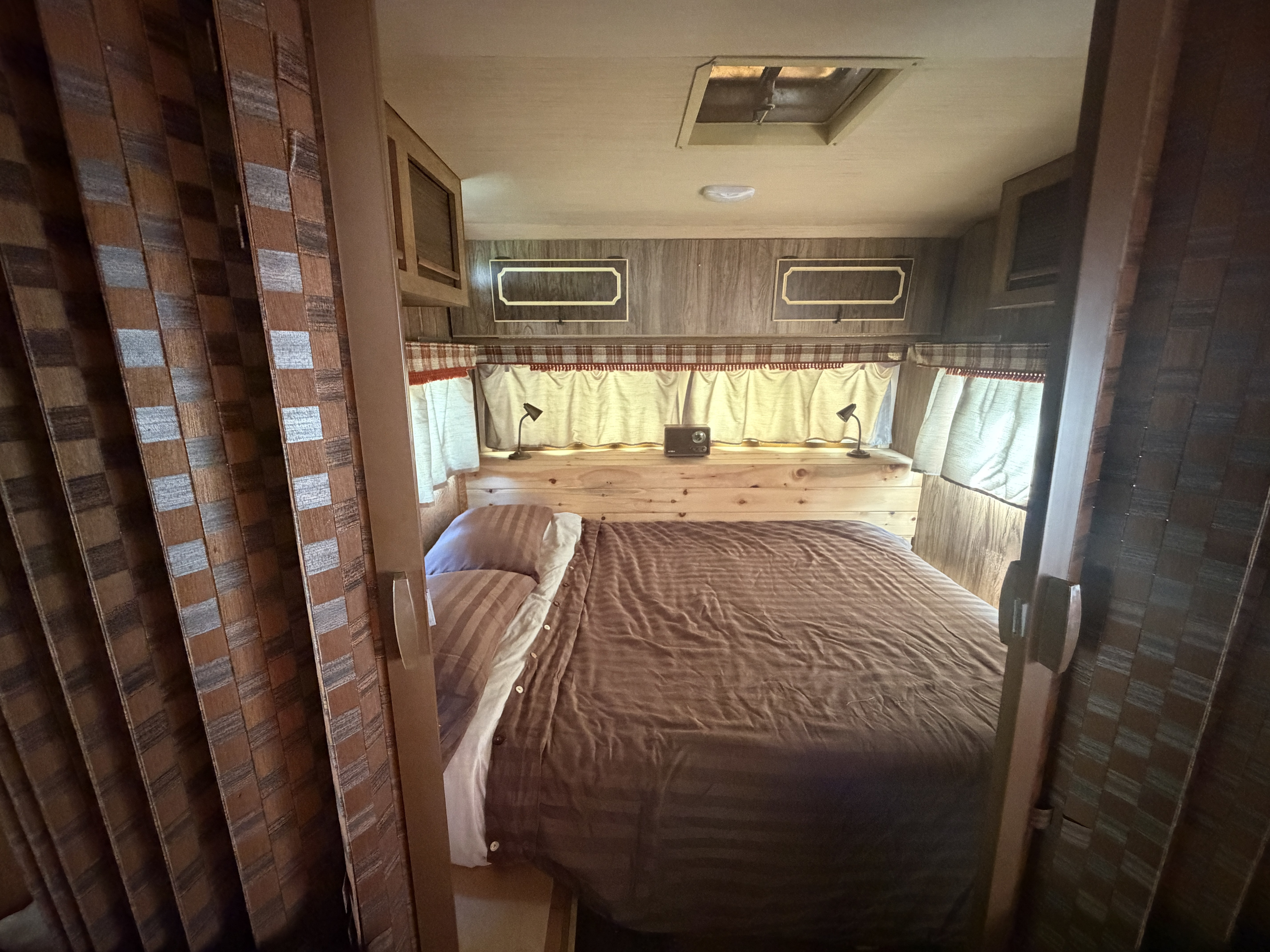 Experience comfort in this RV rental bedroom: a cozy bed, wood paneling, and practical lighting for travel.. Glendale Glendette Deluxe 1978