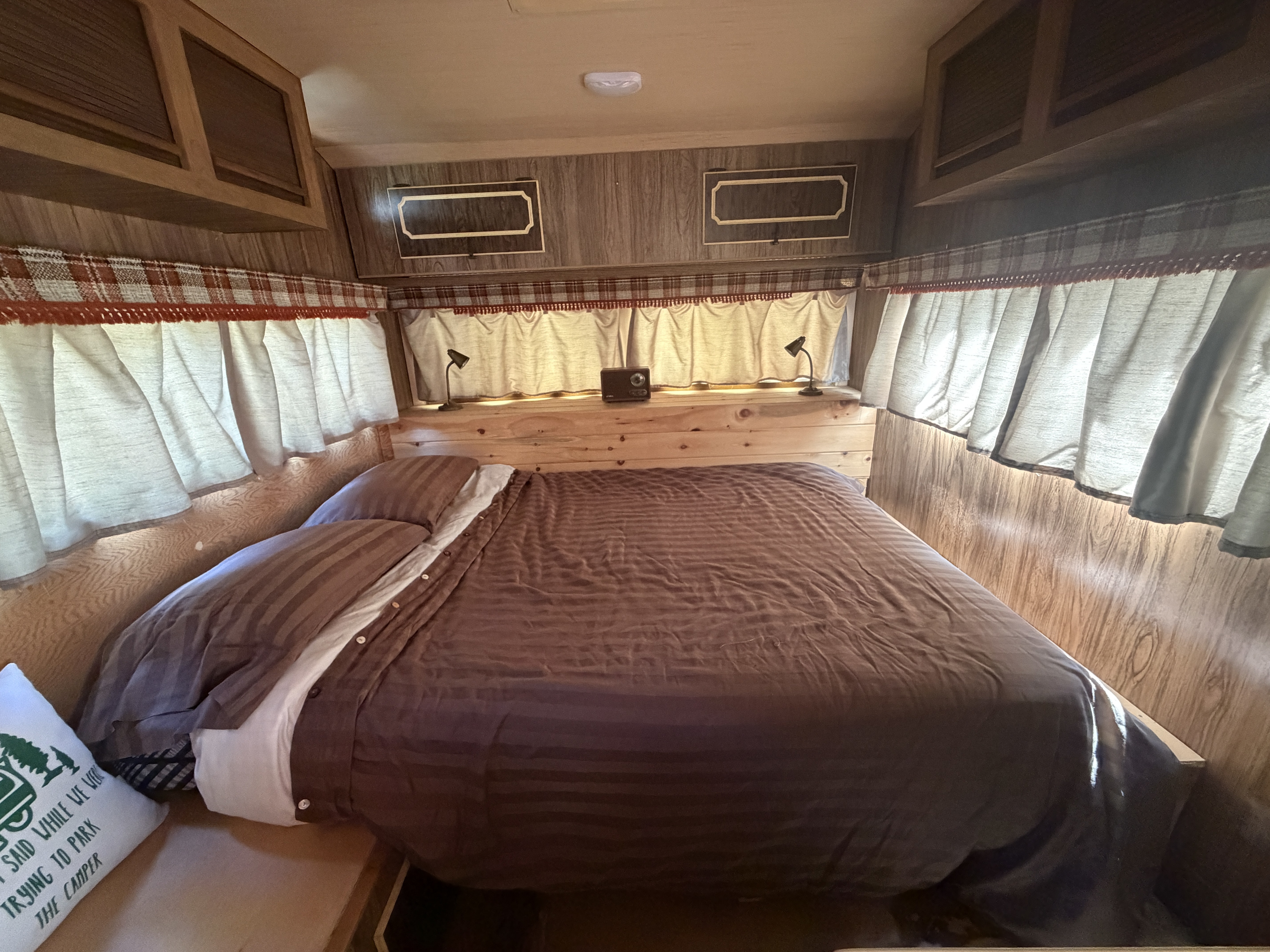 Cozy RV rental bedroom interior featuring a comfortable bed with brown bedding, wooden paneling, and overhead storage.. Glendale Glendette Deluxe 1978
