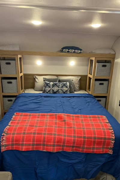 Cozy RV rental bedroom featuring a comfy bed with blue and red blankets, built-in storage, and ambient lighting.. Forest River Cherokee Wolf Den 2024