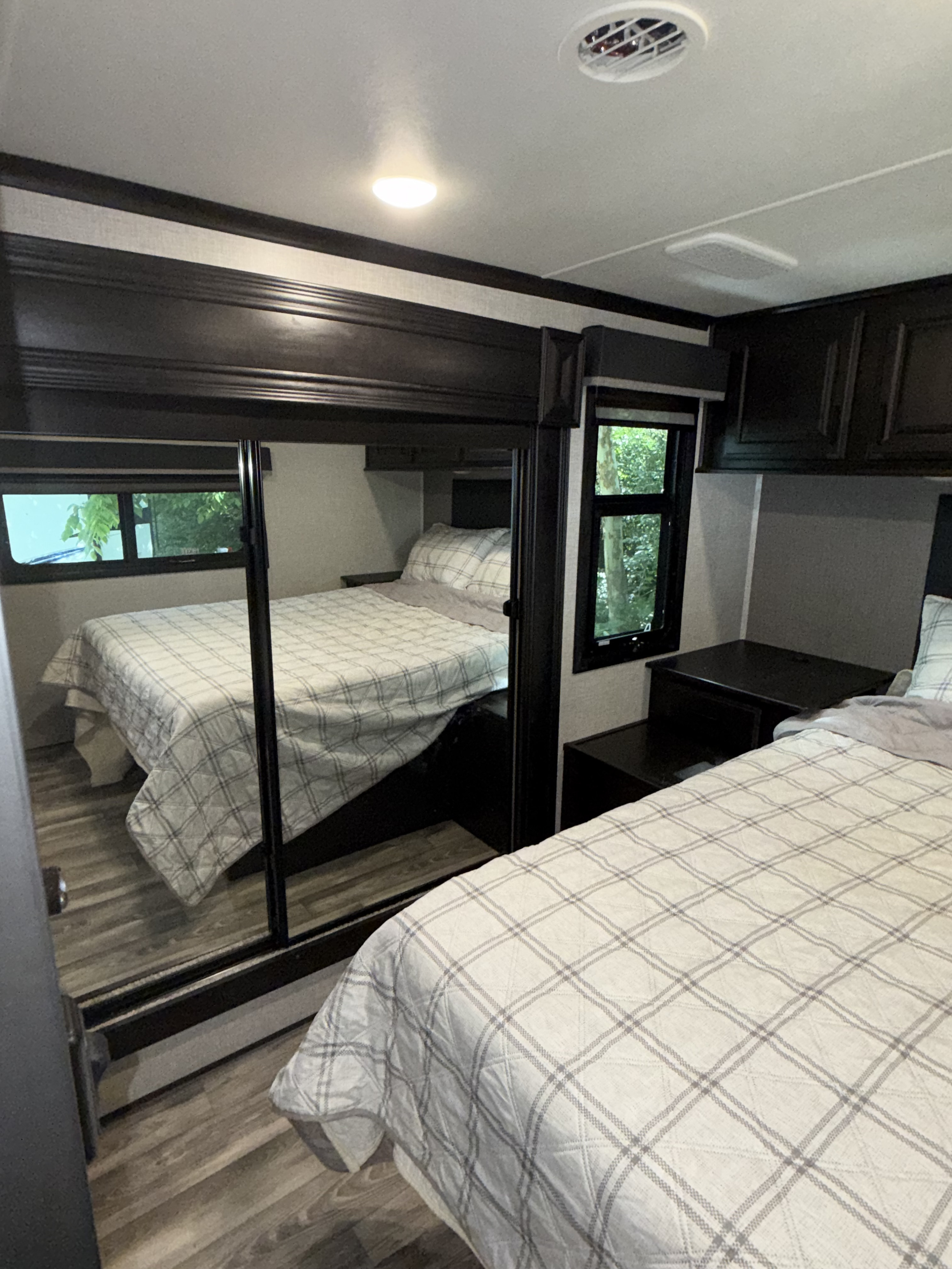Spacious RV rental bedroom featuring two beds with plaid quilts, a mirrored closet, dark wood trim, and a window view.. Highland Ridge RV Open Range 2023